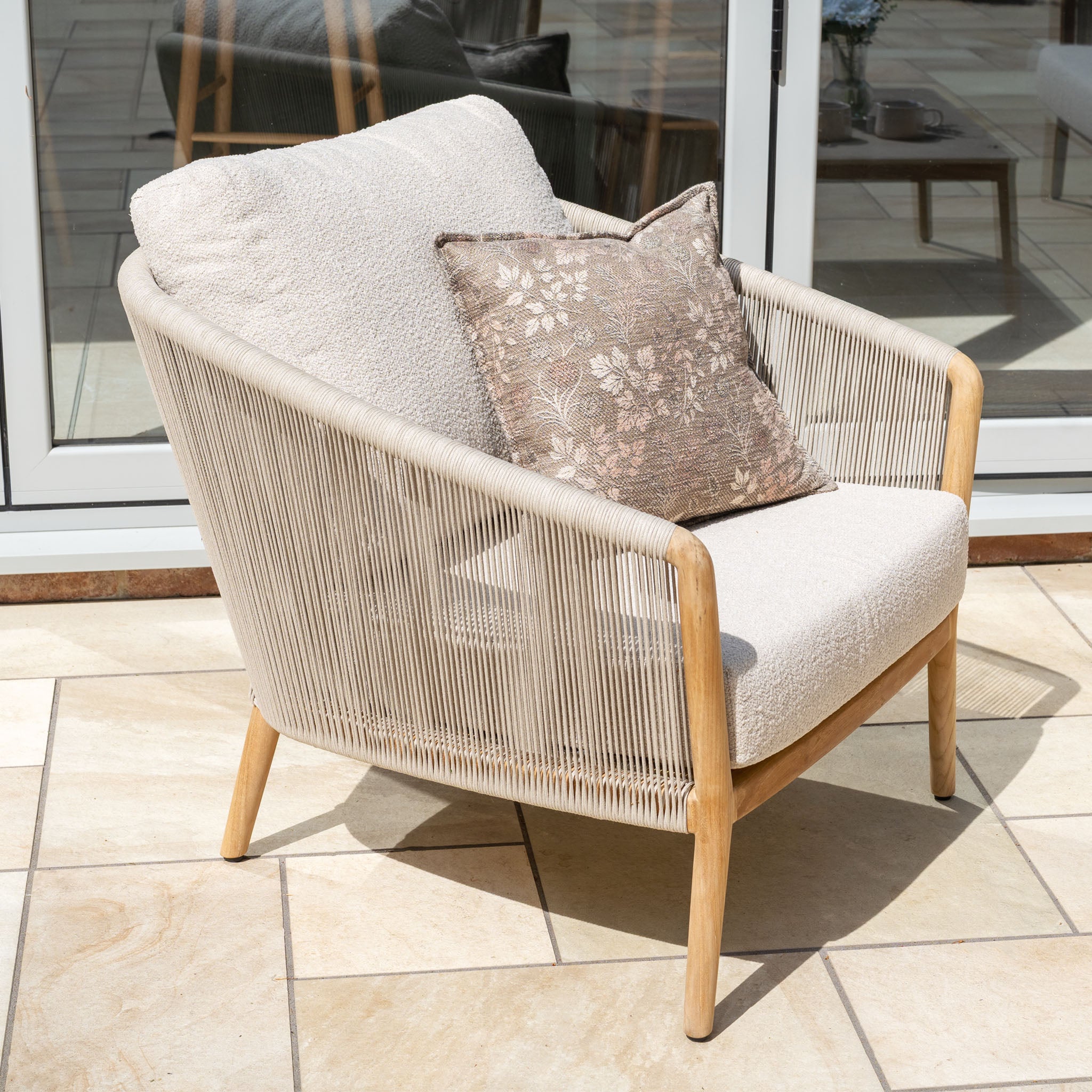 The New York 3 Seat Sofa Set, featuring beige cushions and patterned pillows, adds style to your stone patio by the glass doors—a perfect blend of comfort and weather-resistant design.