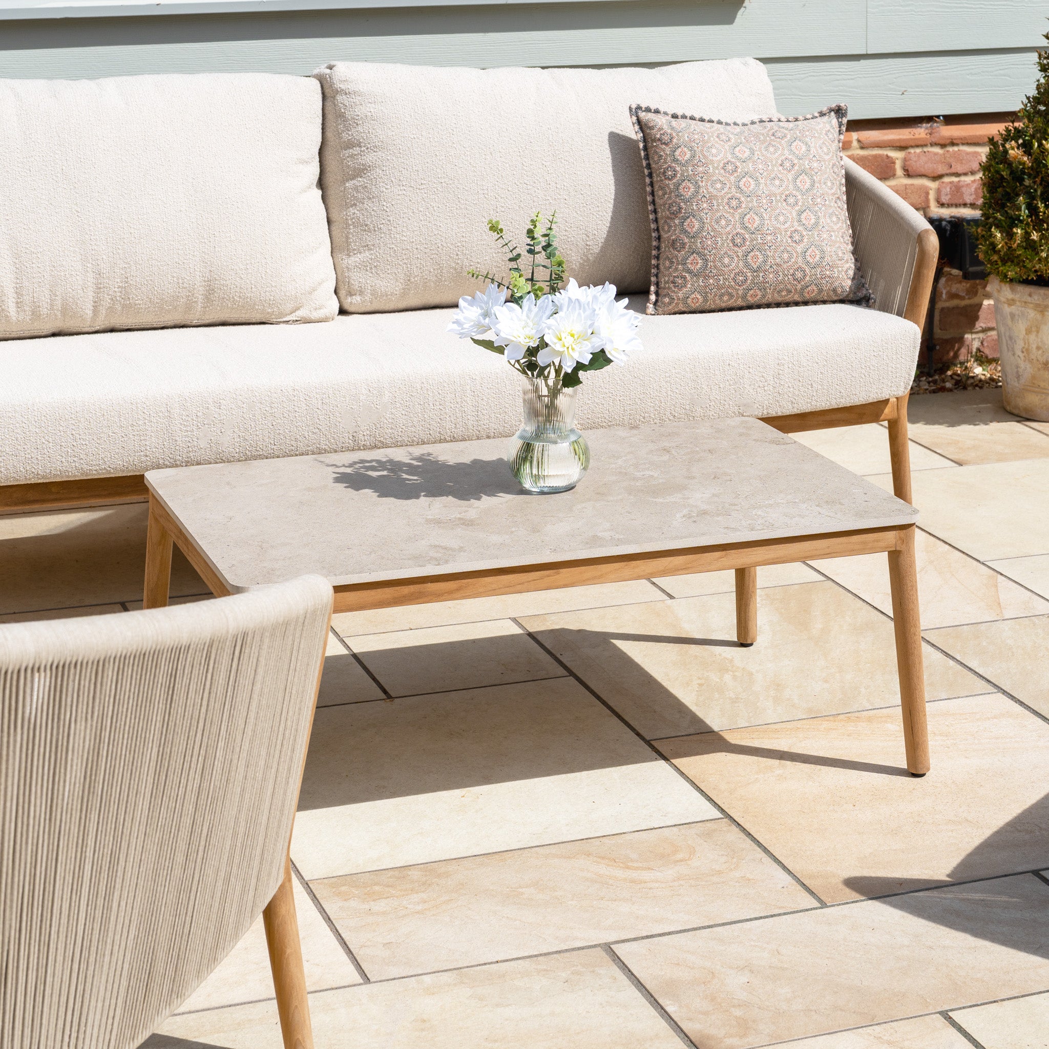 A stylish outdoor patio with the New York 3 Seat Sofa Set and a coffee table, accented by white flowers—combining modern flair and weather-resistant comfort for lasting enjoyment.