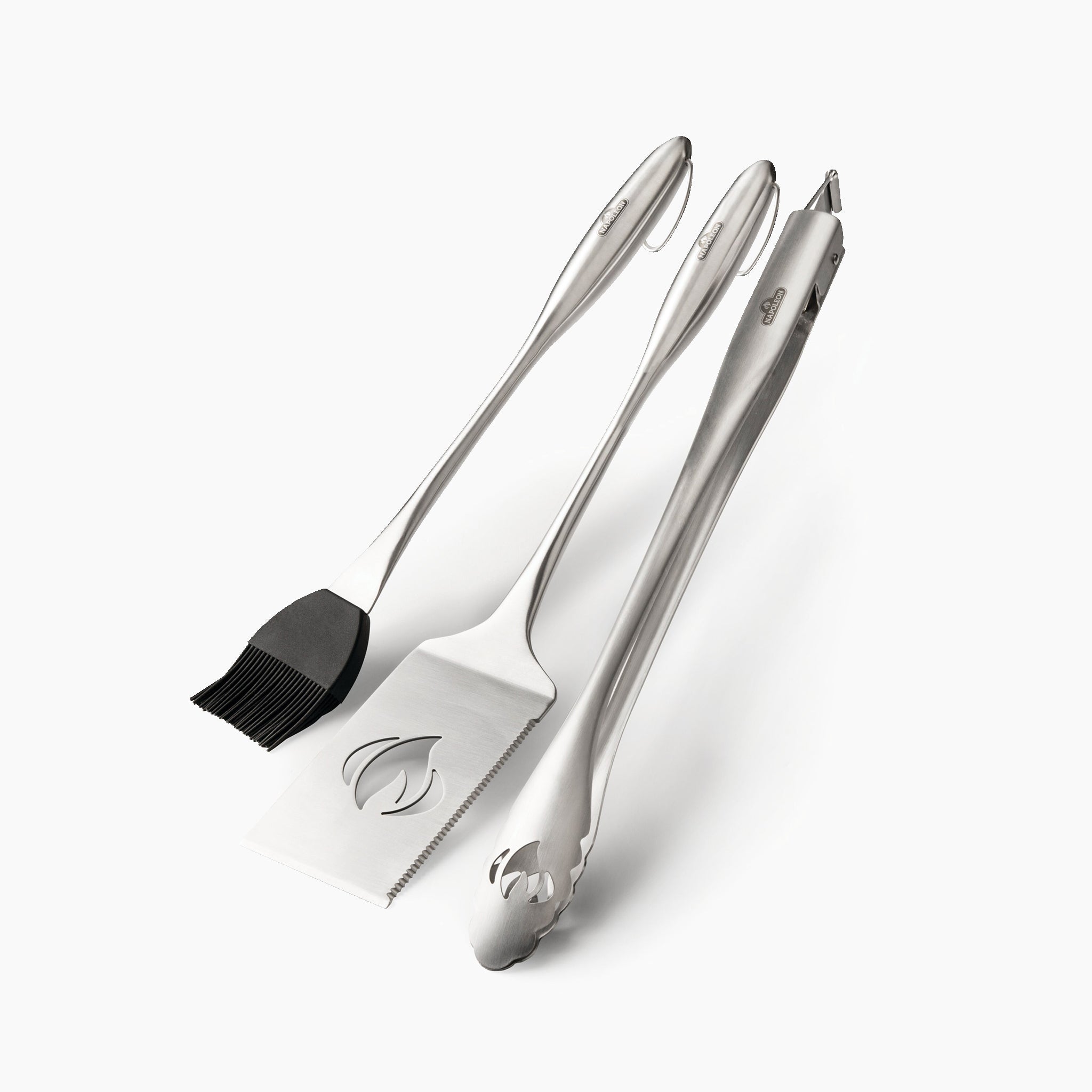 Introducing the Napoleon 3-Piece PRO Stainless Steel Grill Toolset: a trio of exceptional barbecue tools featuring a basting brush, spatula, and tongs. This indispensable grilling accessory guarantees durability and efficiency against a pristine white backdrop.