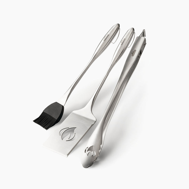 Introducing the Napoleon 3-Piece PRO Stainless Steel Grill Toolset: a trio of exceptional barbecue tools featuring a basting brush, spatula, and tongs. This indispensable grilling accessory guarantees durability and efficiency against a pristine white backdrop.
