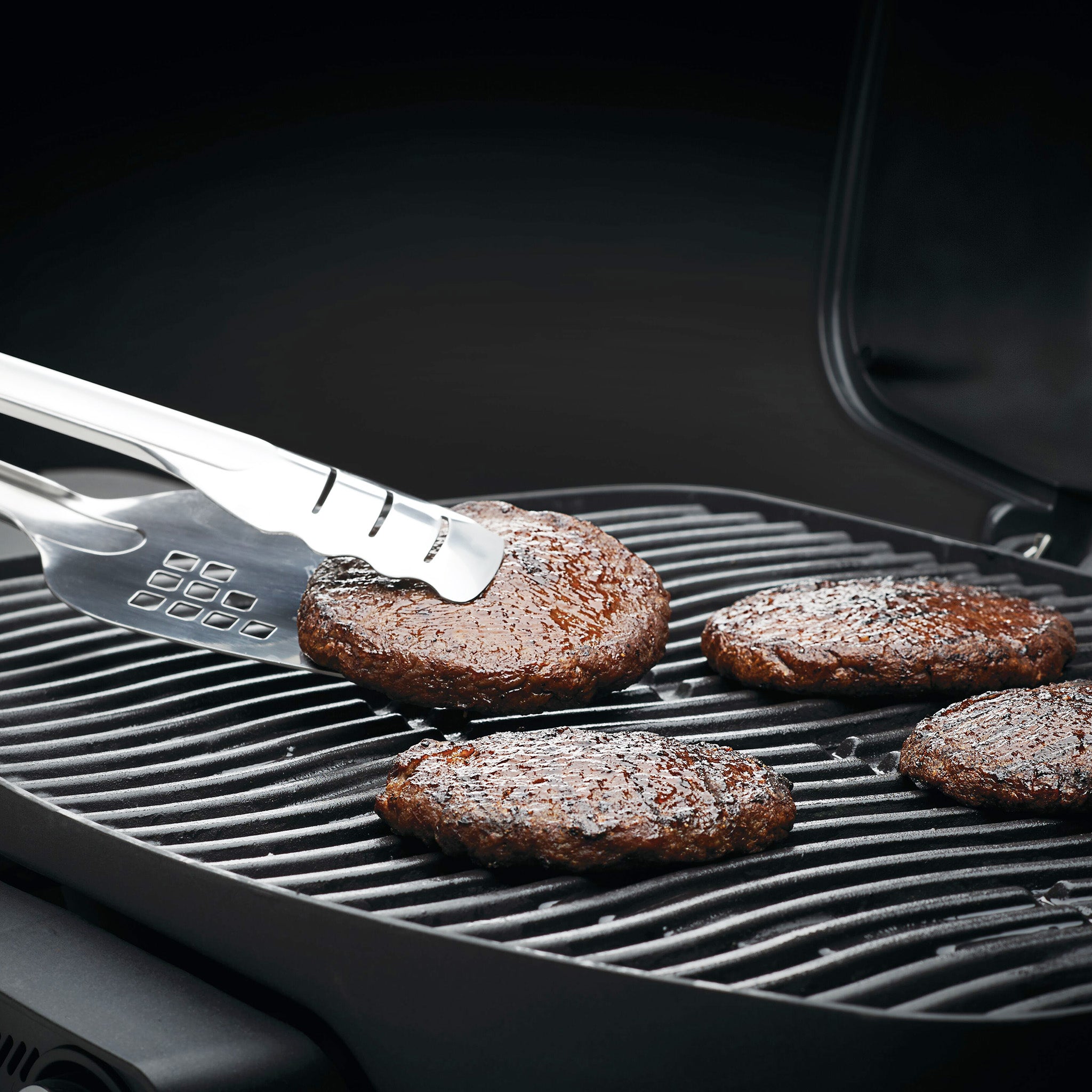 Using a Napoleon Stainless Steel Spatutong, you can effortlessly hold a grilled burger patty over other patties on a hot grill, illustrating its versatility as the ultimate barbecue accessory.