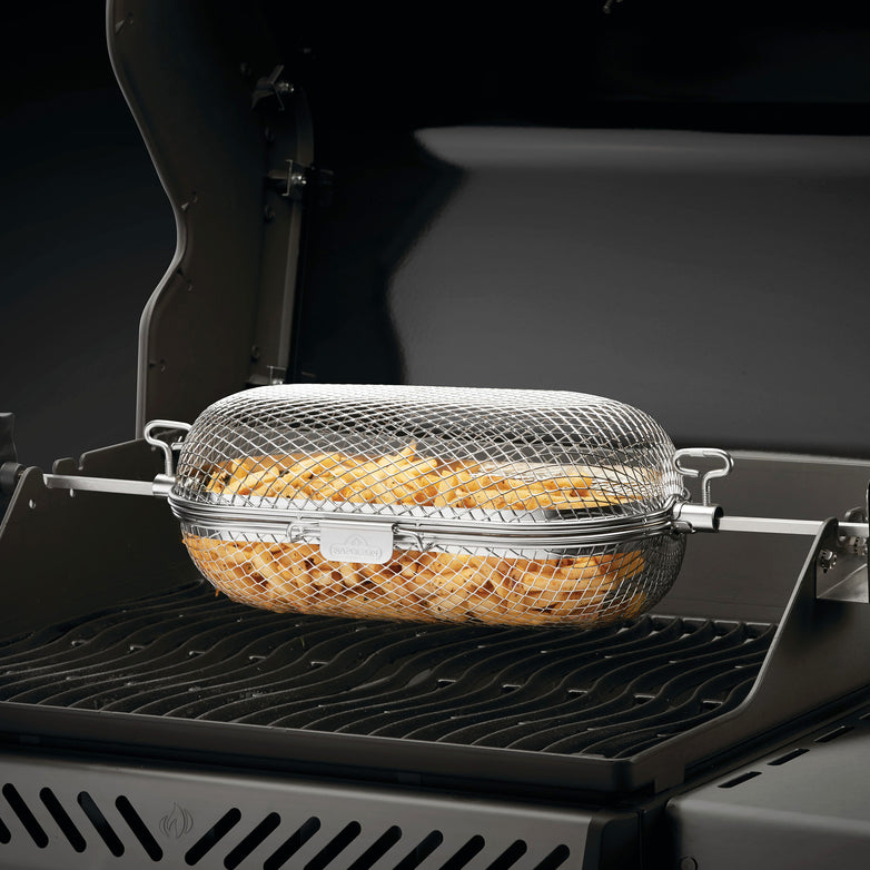 A Napoleon Stainless Steel Rotisserie Basket filled with sliced potatoes is placed on a barbecue grill with the lid open.