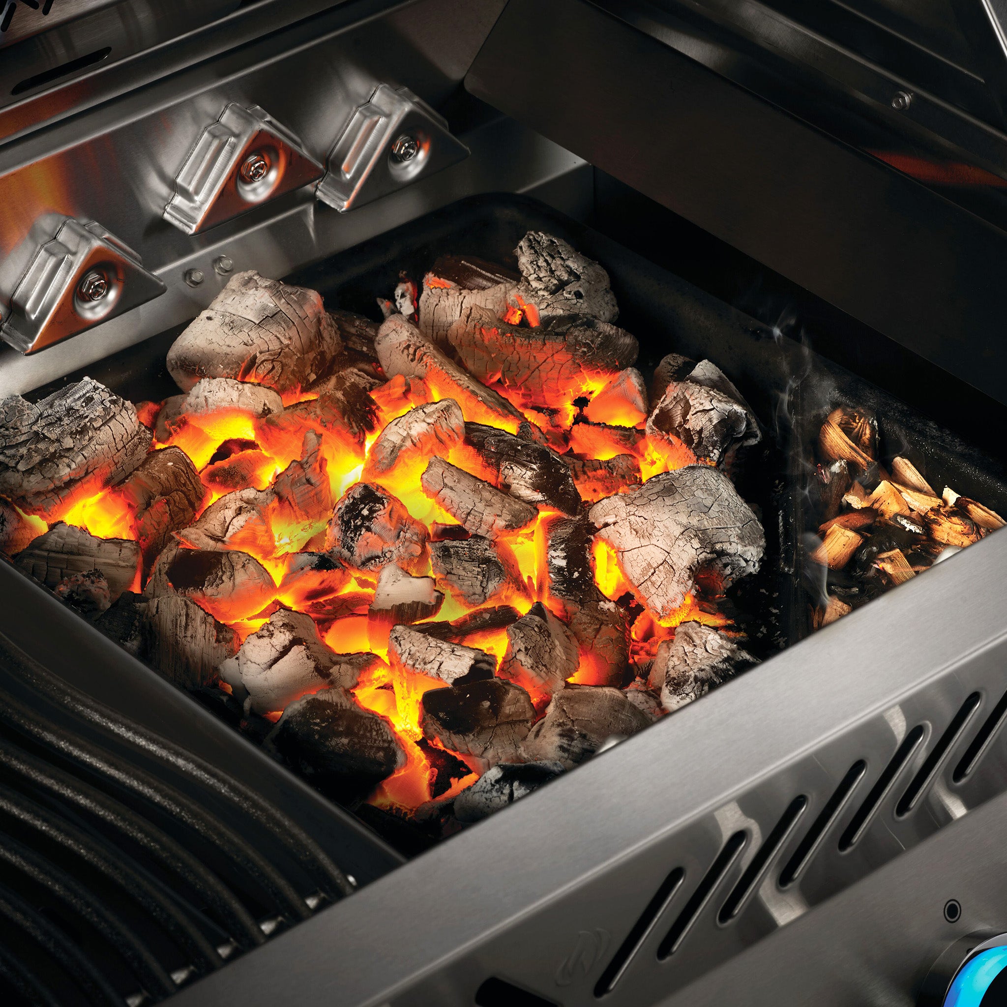 Close-up of glowing charcoal and embers inside a Napoleon Cast Iron Charcoal & Smoker Tray, with the lid partially opened.