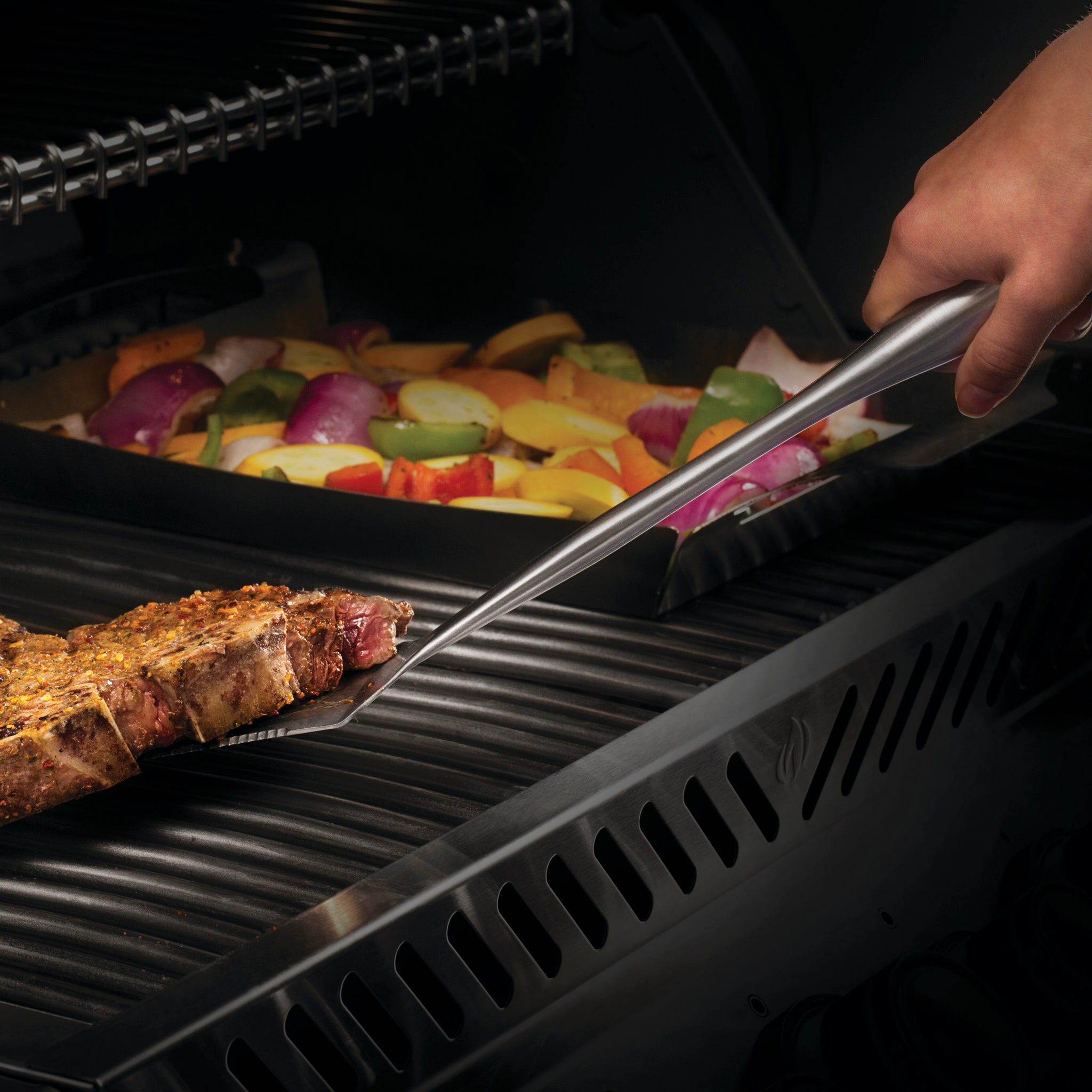 Person grilling seasoned steak and mixed vegetables on an outdoor grill using the Napoleon 3-Piece PRO Stainless Steel Grill Toolset.