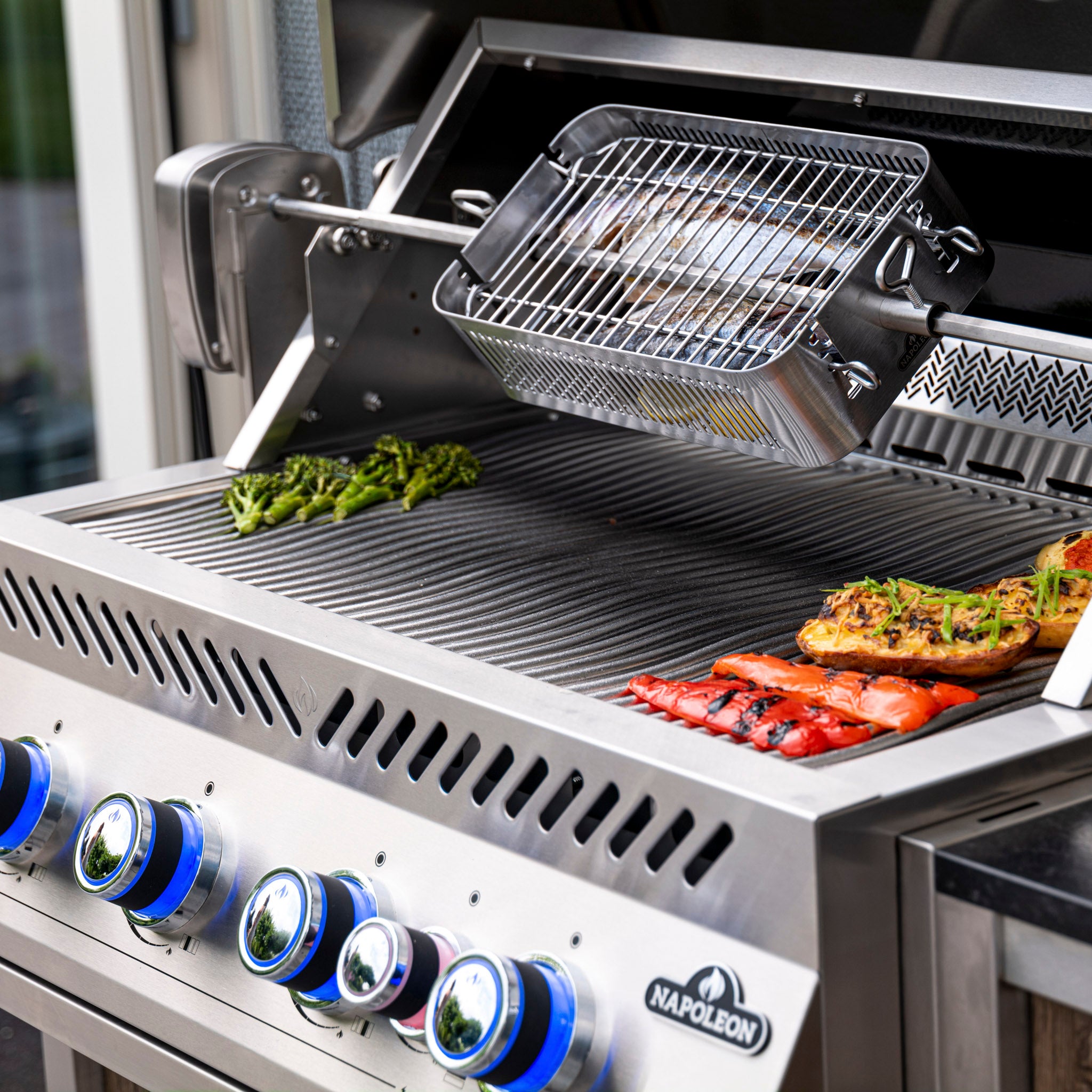 A Napoleon 700 Series 32" Built-in Gas Grill with vegetables, including broccoli and peppers, and fish cooking on it; shiny control knobs in the foreground.