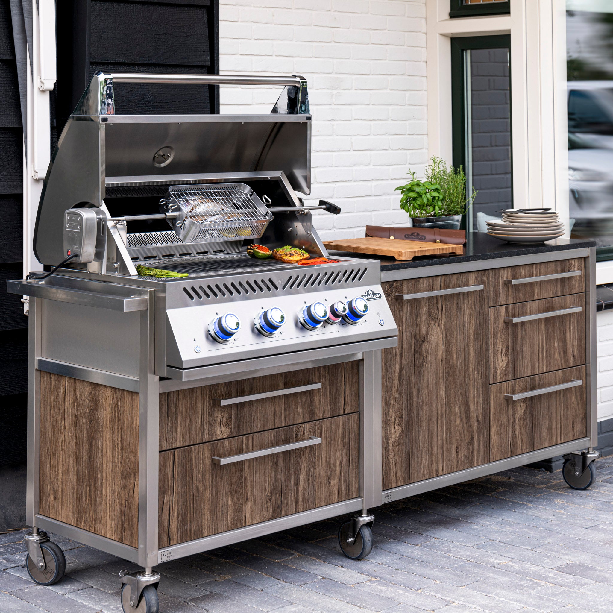 Outdoor kitchen featuring the Napoleon 700 Series 32" Built-in Gas Grill, wooden cabinets, and a countertop adorned with plates and potted herbs.