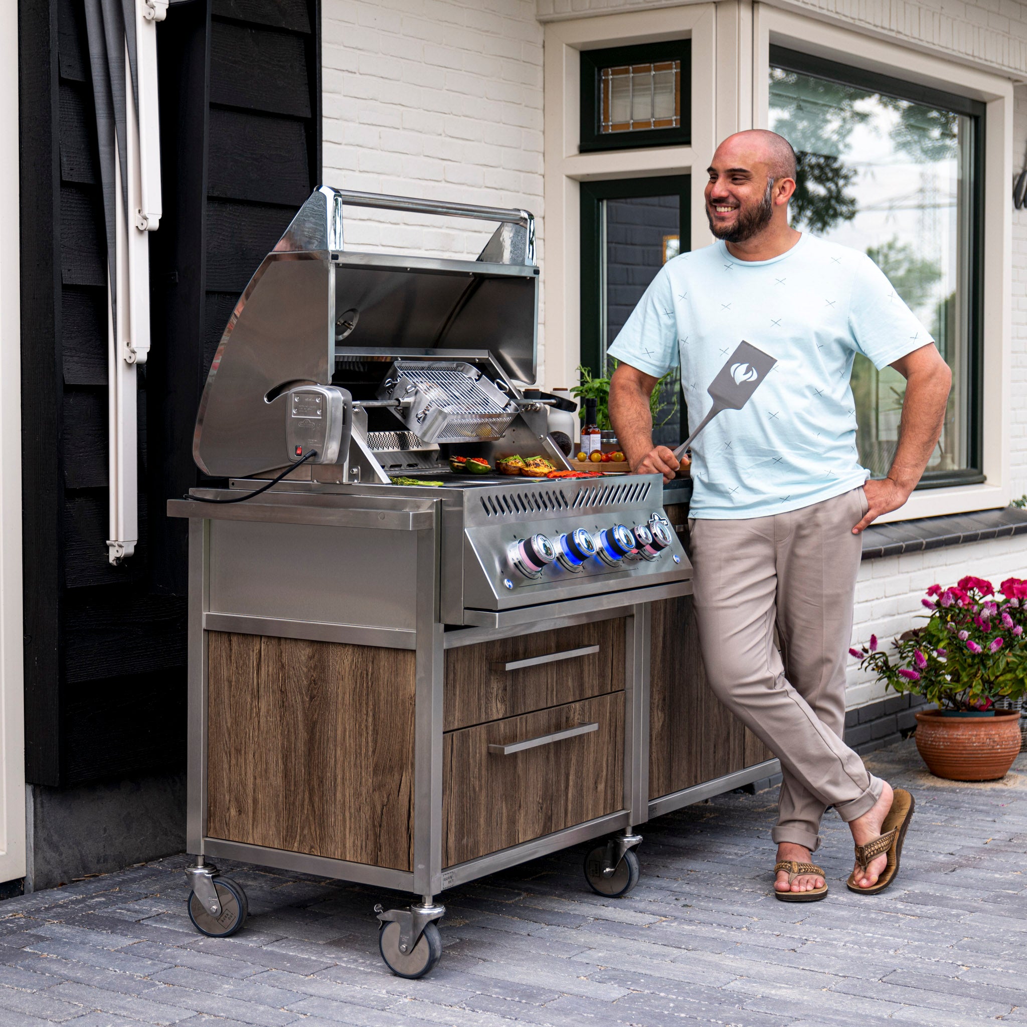 A man standing beside the Napoleon 700 Series 32" Built-in Gas Grill on a patio, holding a spatula and smiling.