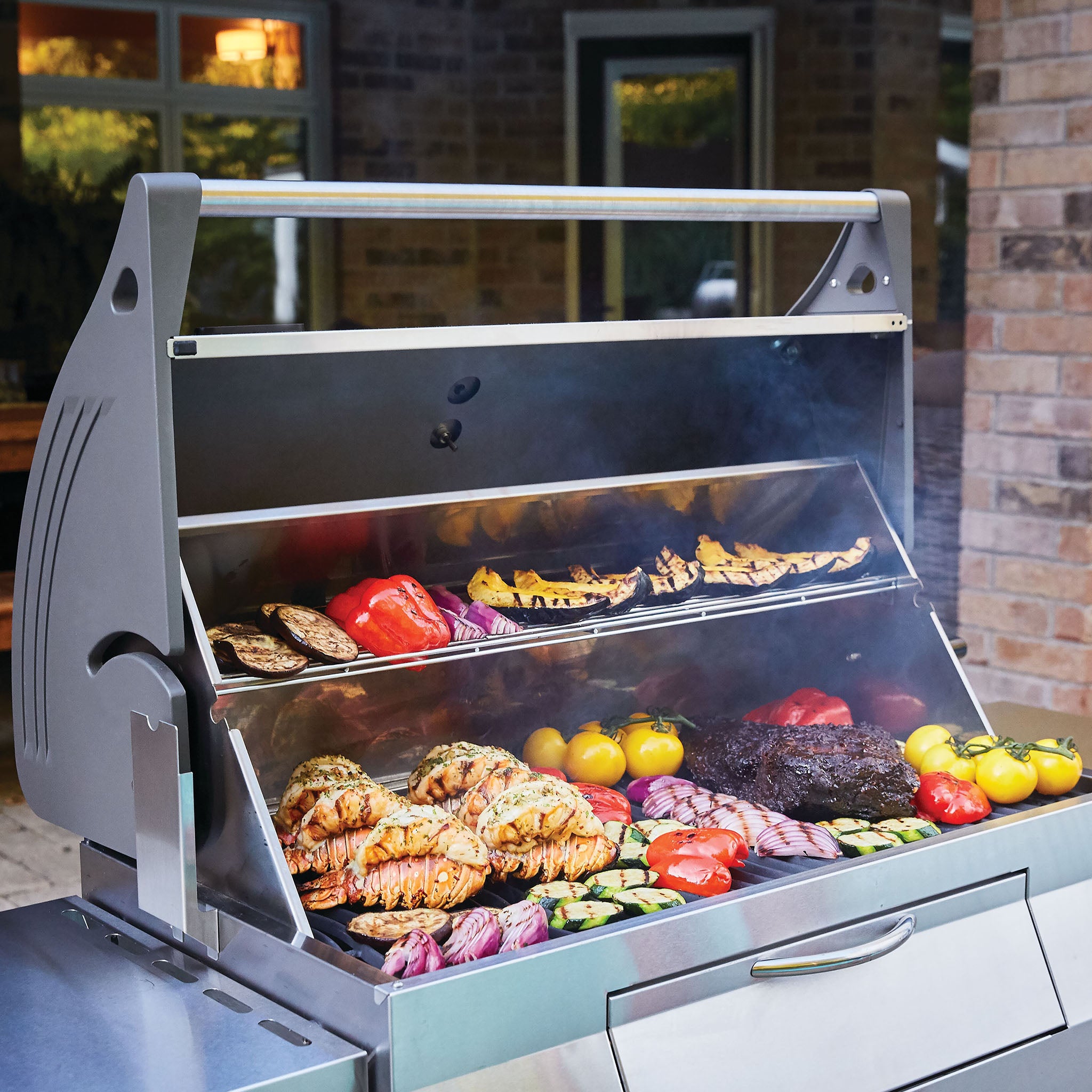 A variety of vegetables and meats sizzle on the Napoleon Charcoal Professional Barbecue, a stainless steel charcoal grill, in an outdoor setting.