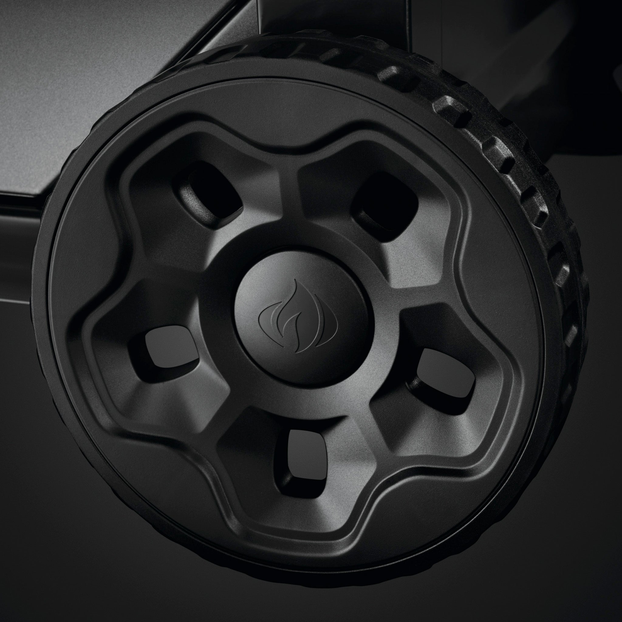 A close-up shot of a wheel features black plastic construction with a flame symbol at the center and a textured tire rim, evocative of the Napoleon Freestyle 365 Gas Barbecue's JETFIRE ignition system.