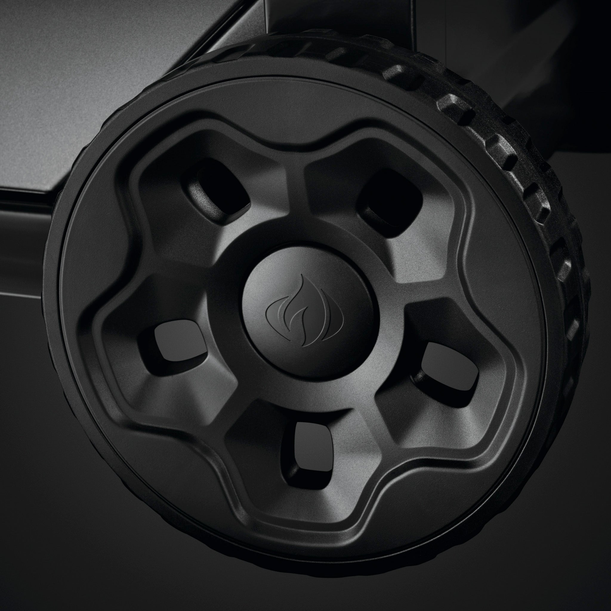 Close-up of a black, five-spoke wheel with a flame-like logo in the center, attached to a piece of machinery on the Napoleon Freestyle 425 Gas Barbecue.
