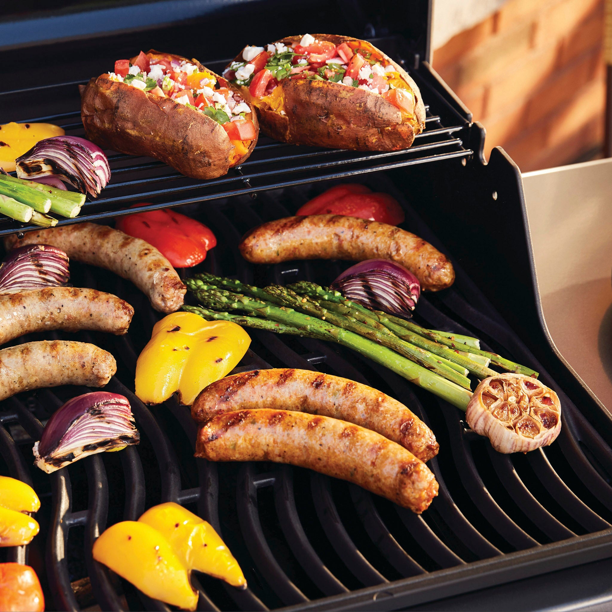 Grill sausages, asparagus, bell peppers, garlic, onions, and stuffed bread on the rack of a Napoleon Freestyle 365 Gas Barbecue.