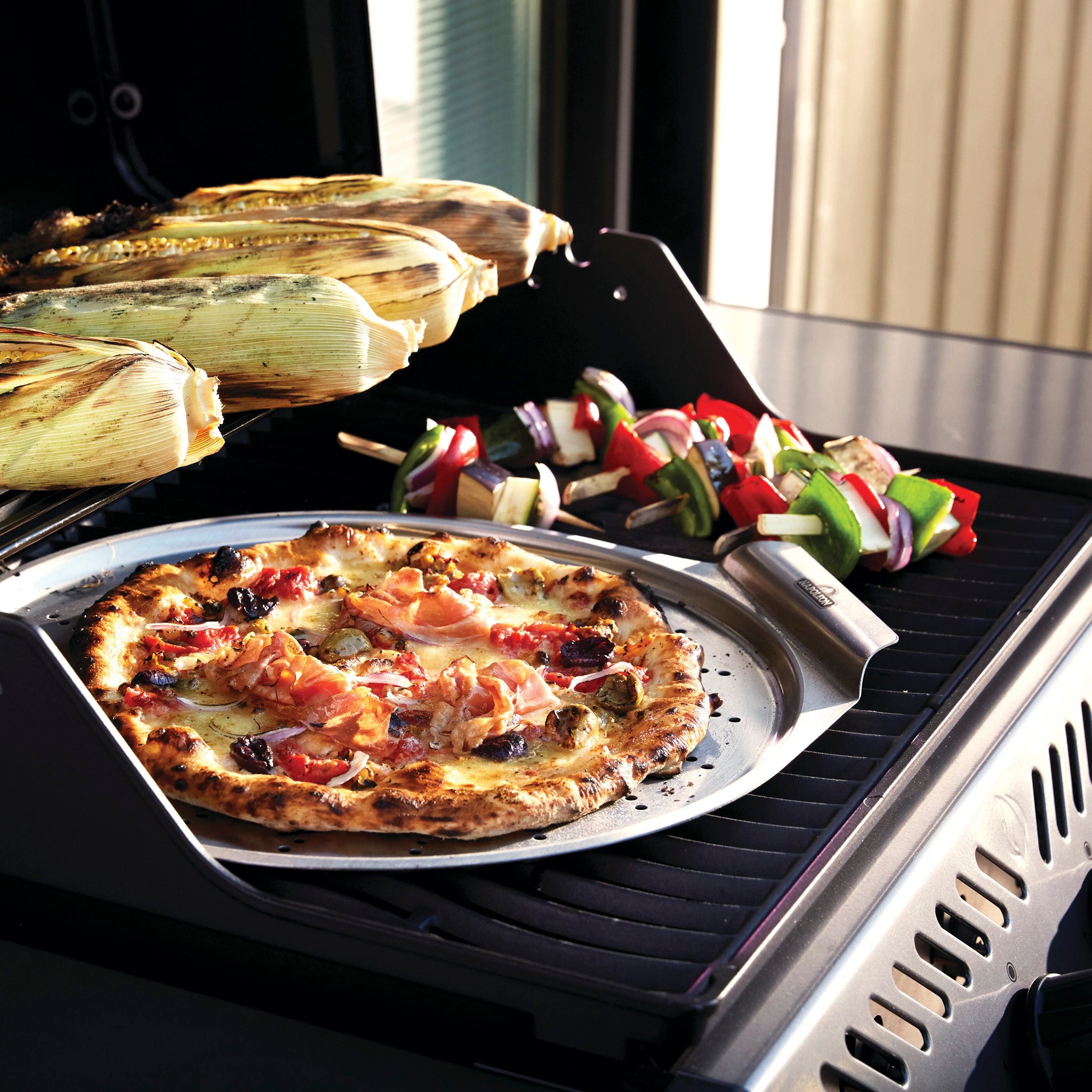 Pizza, corn, and vegetable skewers sizzling on a Napoleon Freestyle 425 Gas Barbecue with cast iron porcelainized enamel cooking grids.