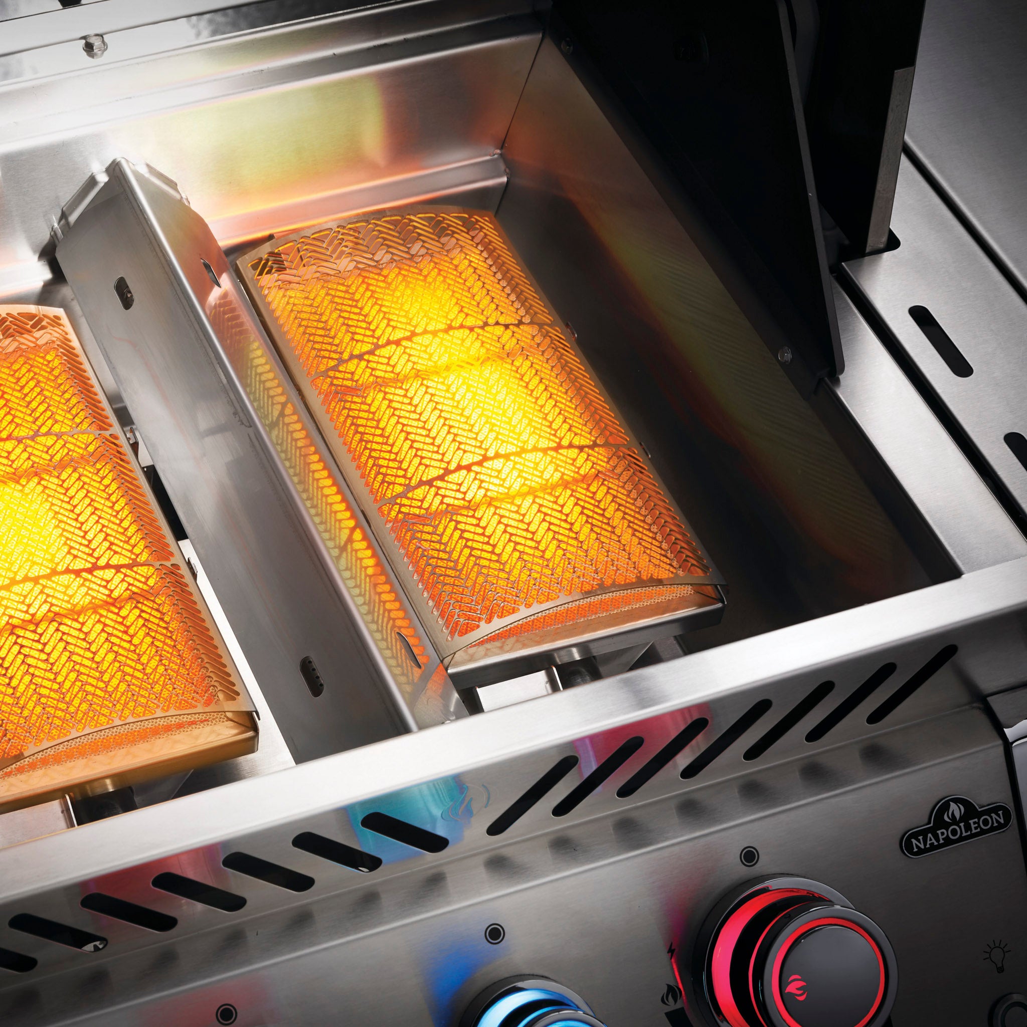 Close-up of an active Napoleon Prestige Pro 825 RSIB Gas Barbecue with glowing infrared burners and control knobs illuminated in blue and red.