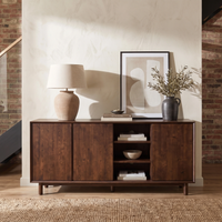 The Oslo 3 Door Sideboard with Shelves in Walnut is styled with a lamp, framed artwork, a vase with branches, and bowls on display against a light wall.