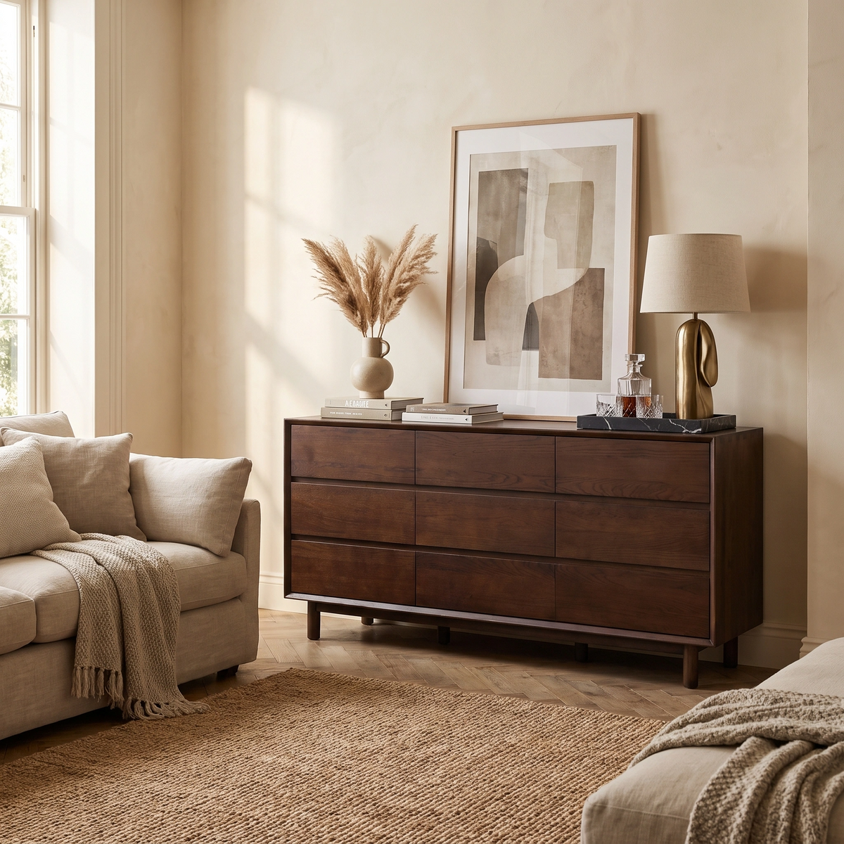 Beige living room with a sofa, lamp, abstract art, woven rug, and an elegant Oslo 9 Drawer Chest in Walnut that adds a touch of stylish walnut bedroom furniture to the space.