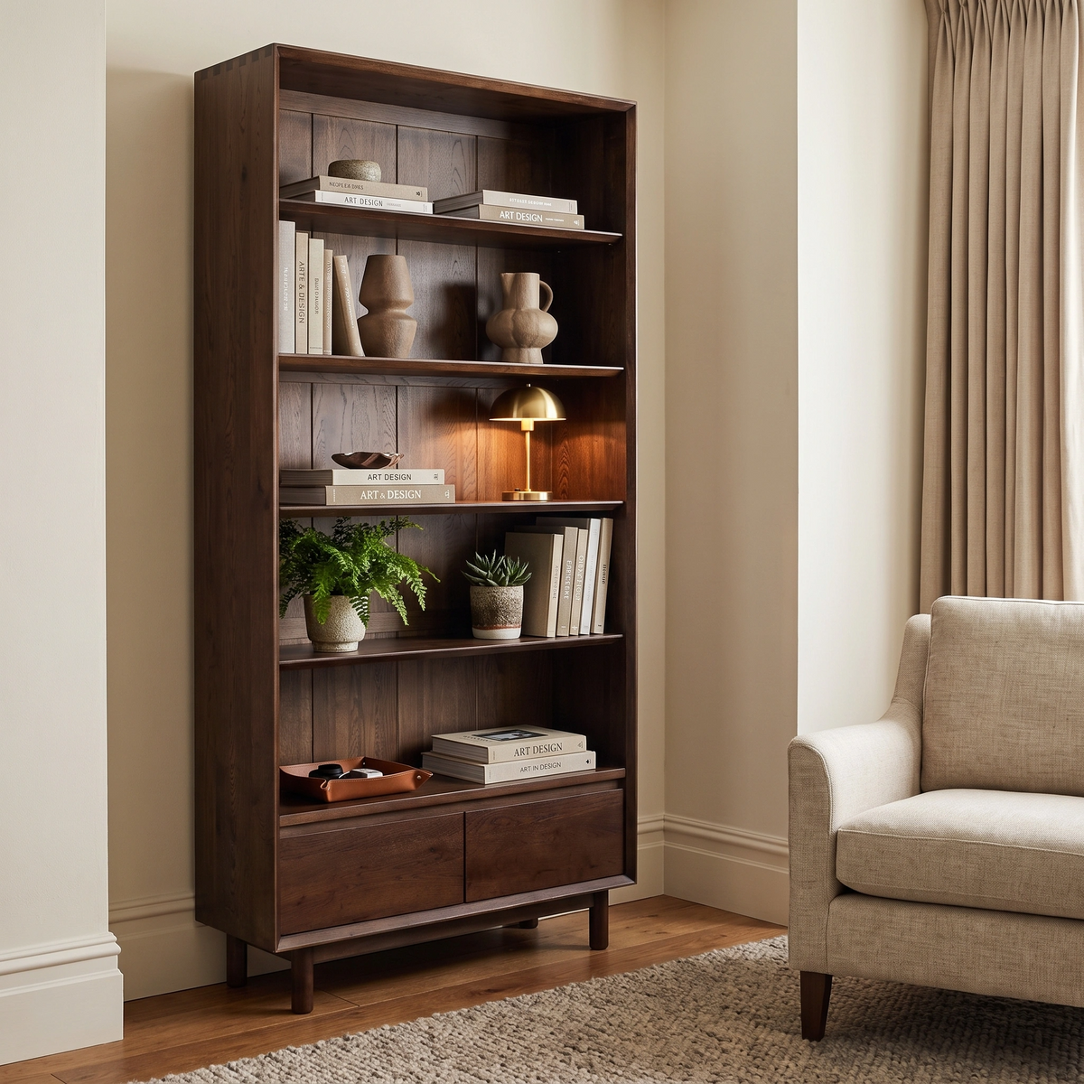 Oslo Bookcase in Walnut styled with books, plants, and decor stands beside a beige armchair in a well-lit room.