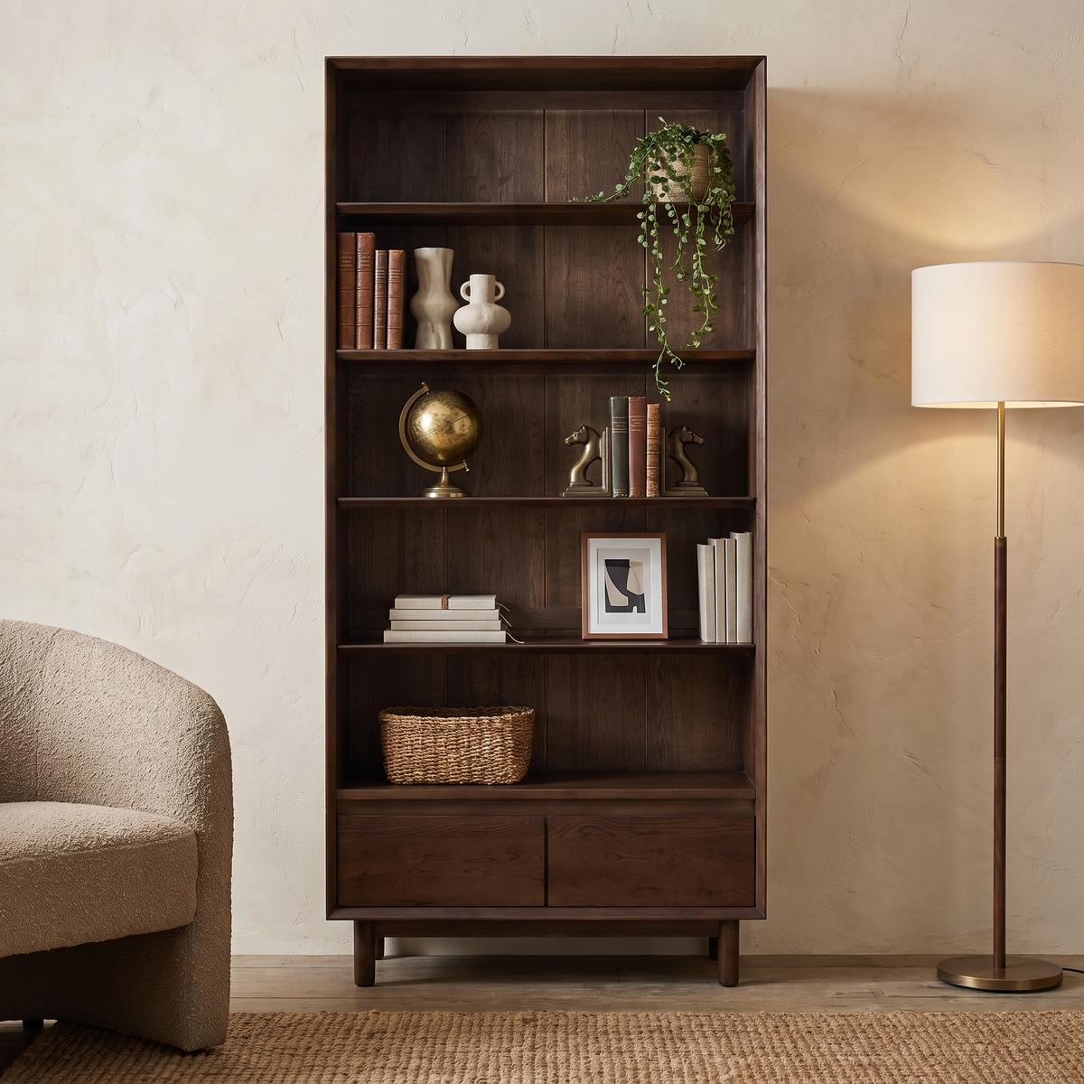Oslo Bookcase in Walnut styled with decor items, positioned beside a floor lamp and a textured beige armchair in a cozy room.