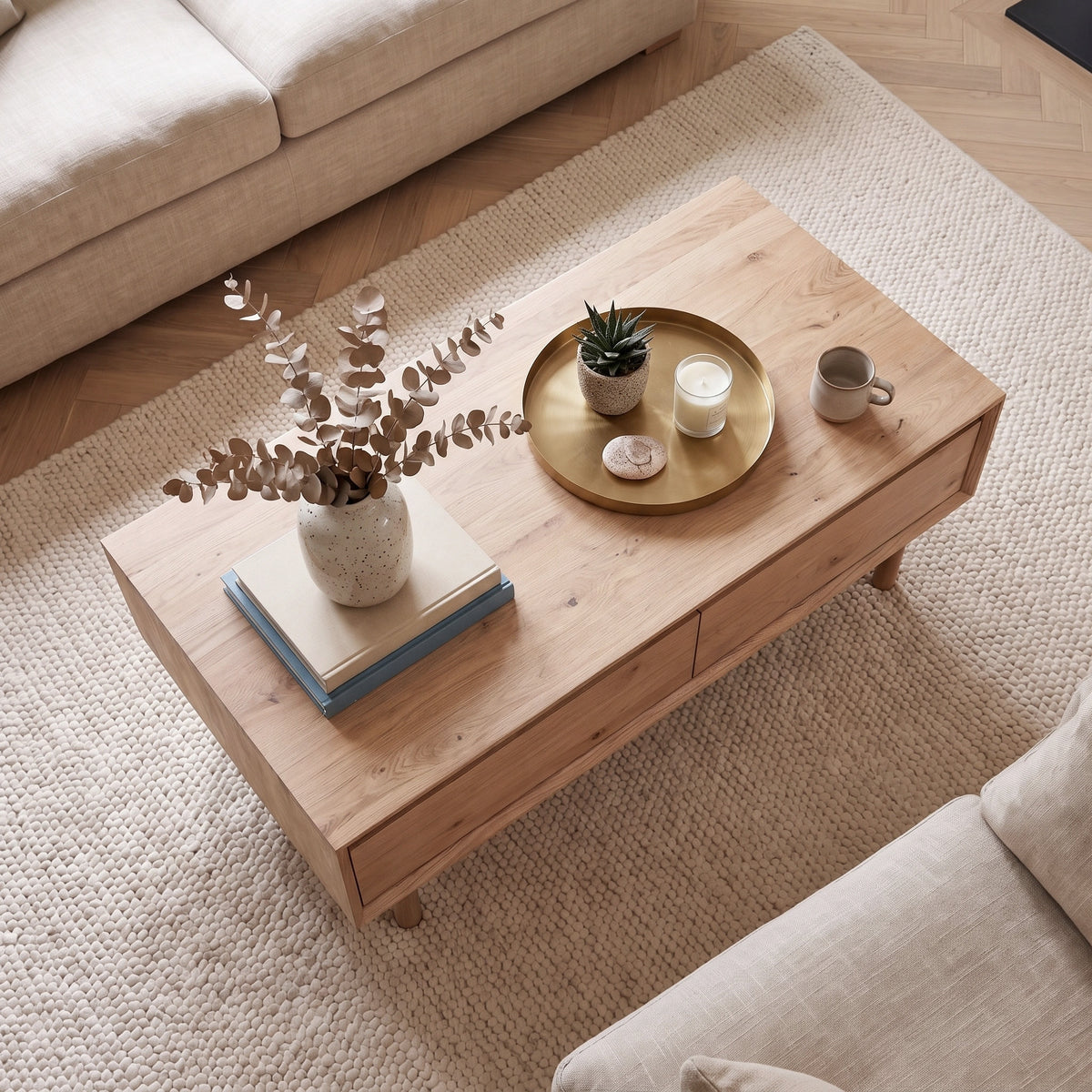 Oslo Coffee Table with 4 Drawers in Light Oak, beautifully styled with decor—vase, books, tray, candle, plant, and mug—all arranged atop a textured beige rug.