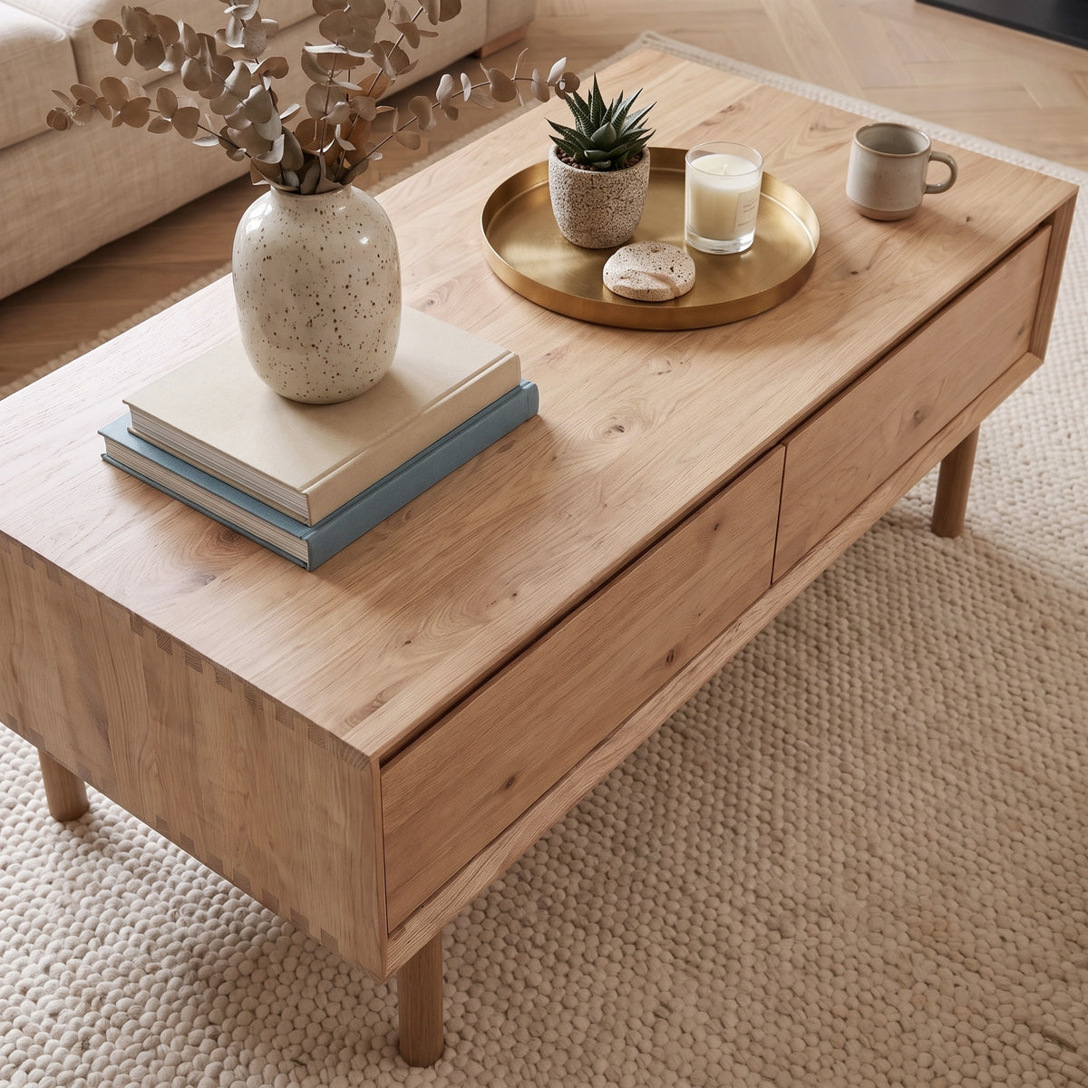 Oslo Coffee Table with 4 Drawers in Light Oak styled with books, a tray, mug, candle, plant, and vase on a cream rug.