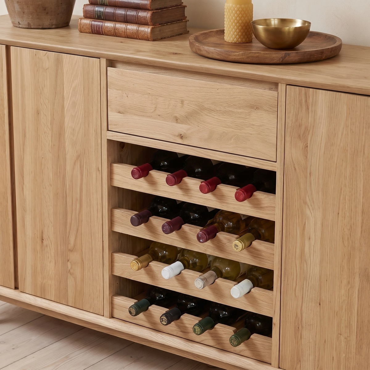The Oslo Grand 4 Door Sideboard with Wine Rack in Light Oak features shelves for storing wine bottles as well as space to display stacked books, a candle, and a brass bowl on top—creating a refined touch to your space.