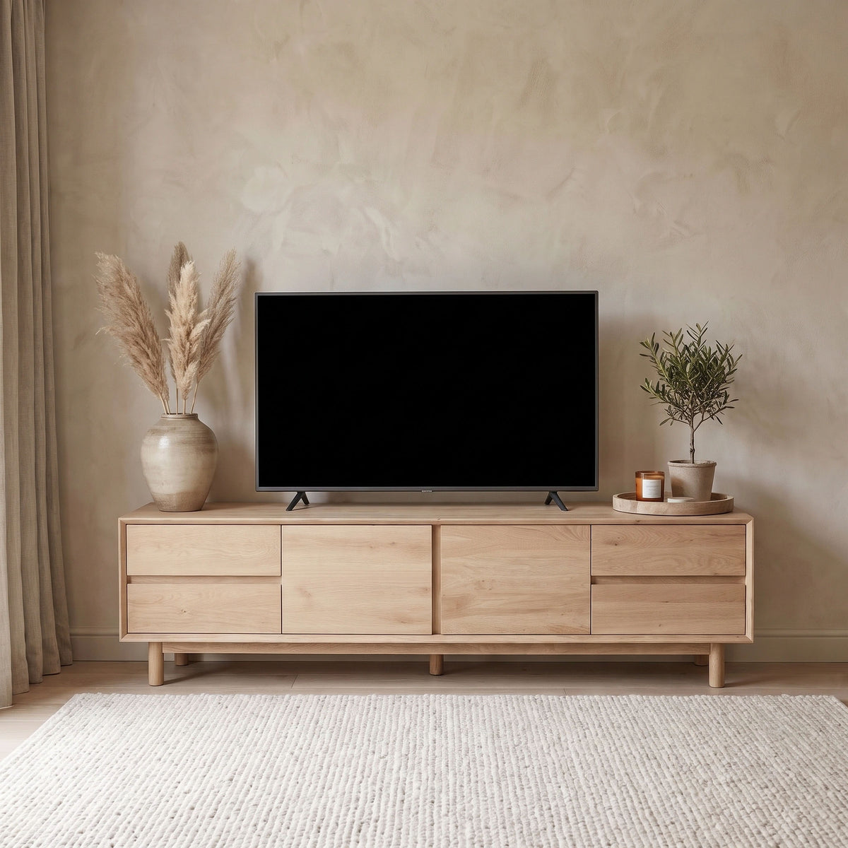 The Oslo TV Unit in Light Oak serves as a stylish base for a flat-screen TV, paired with dried pampas grass, candles, and a potted plant in a neutral room—effortlessly blending modern living room furniture style into any space.