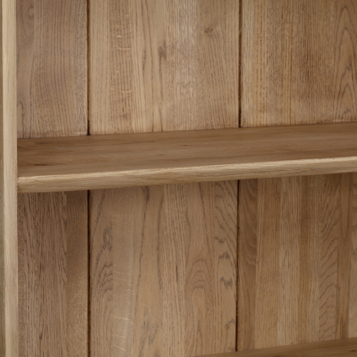 A light oak Oslo Bookcase with a natural finish stands empty against a backdrop of vertical wooden panels, showcasing its timeless design.