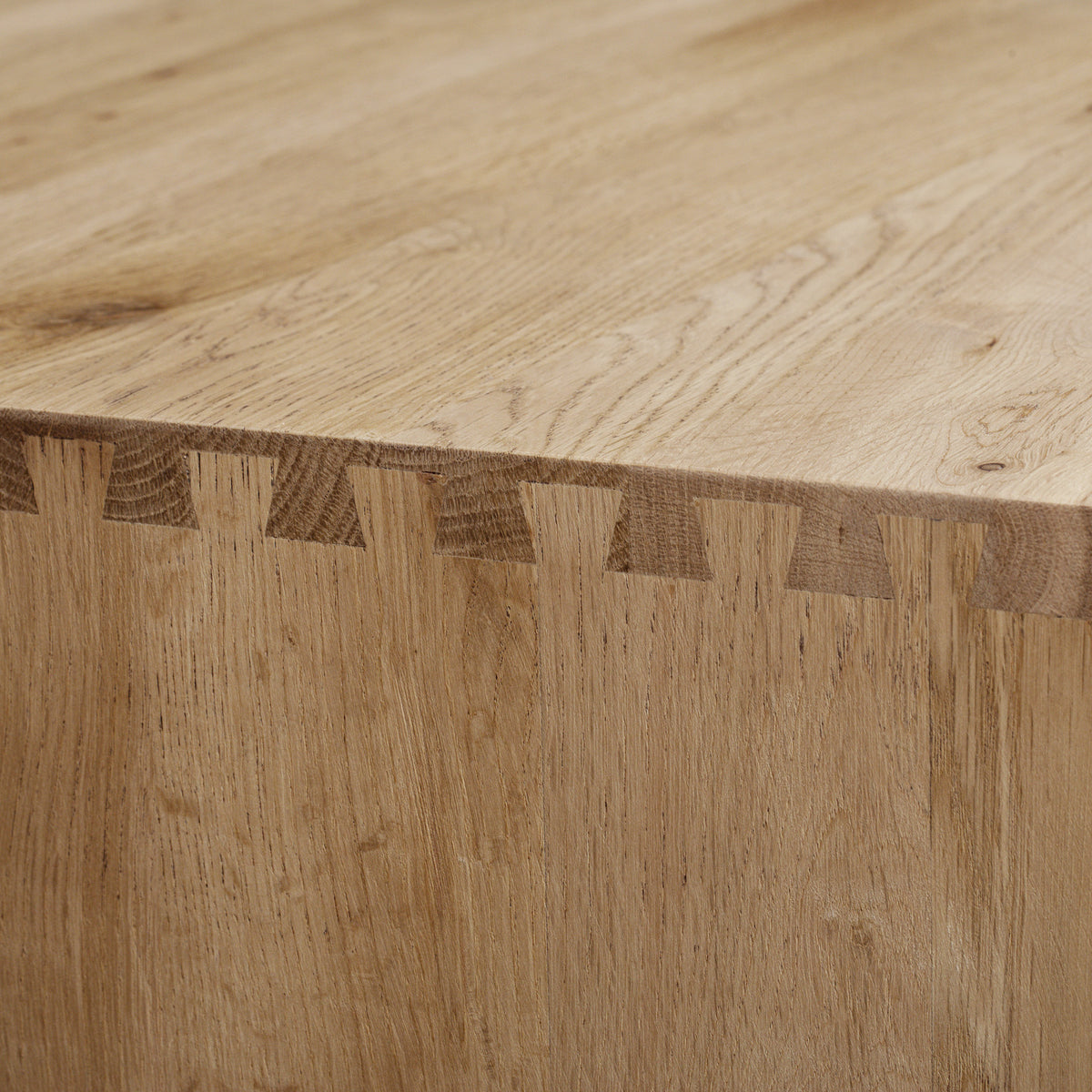 Close-up of a wooden table corner showing dovetail joints and a smooth, natural wood grain finish—an elegant detail often found in modern living room furniture such as the Oslo TV Unit in Light Oak.