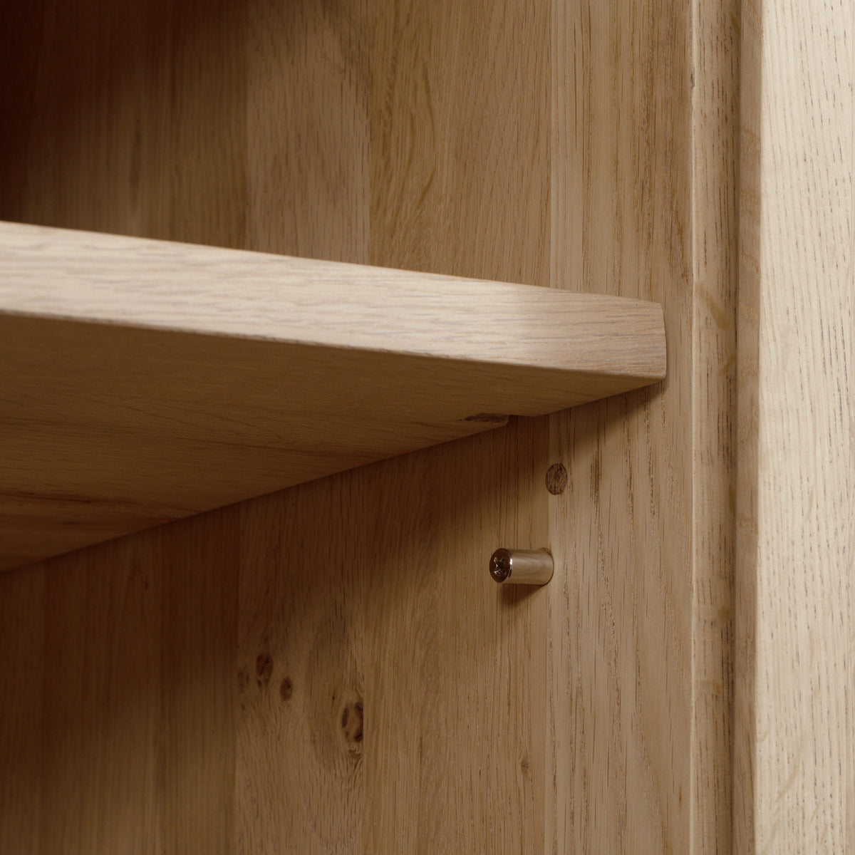 A close-up of a wooden shelf with a metal support pin partially inserted in the side panel, highlighting the adjustable shelving feature of the Oslo 3 Door Sideboard with Shelves in Light Oak.