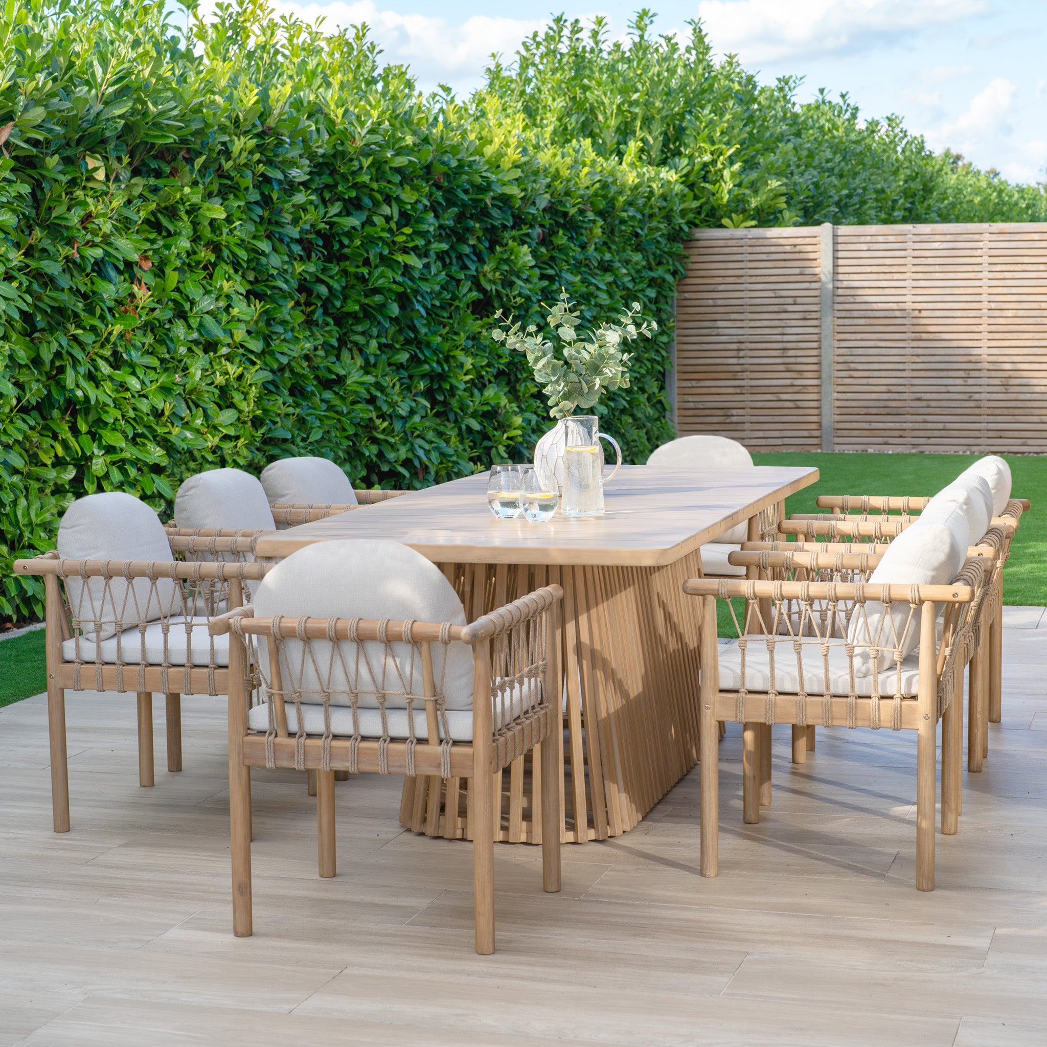 The Paia 8 Seat Rectangular Dining Set in Linen includes eight cushioned chairs with water-resistant polyester fabric and a sustainably sourced Acacia wood table, ideal for alfresco dining on your patio amidst greenery.