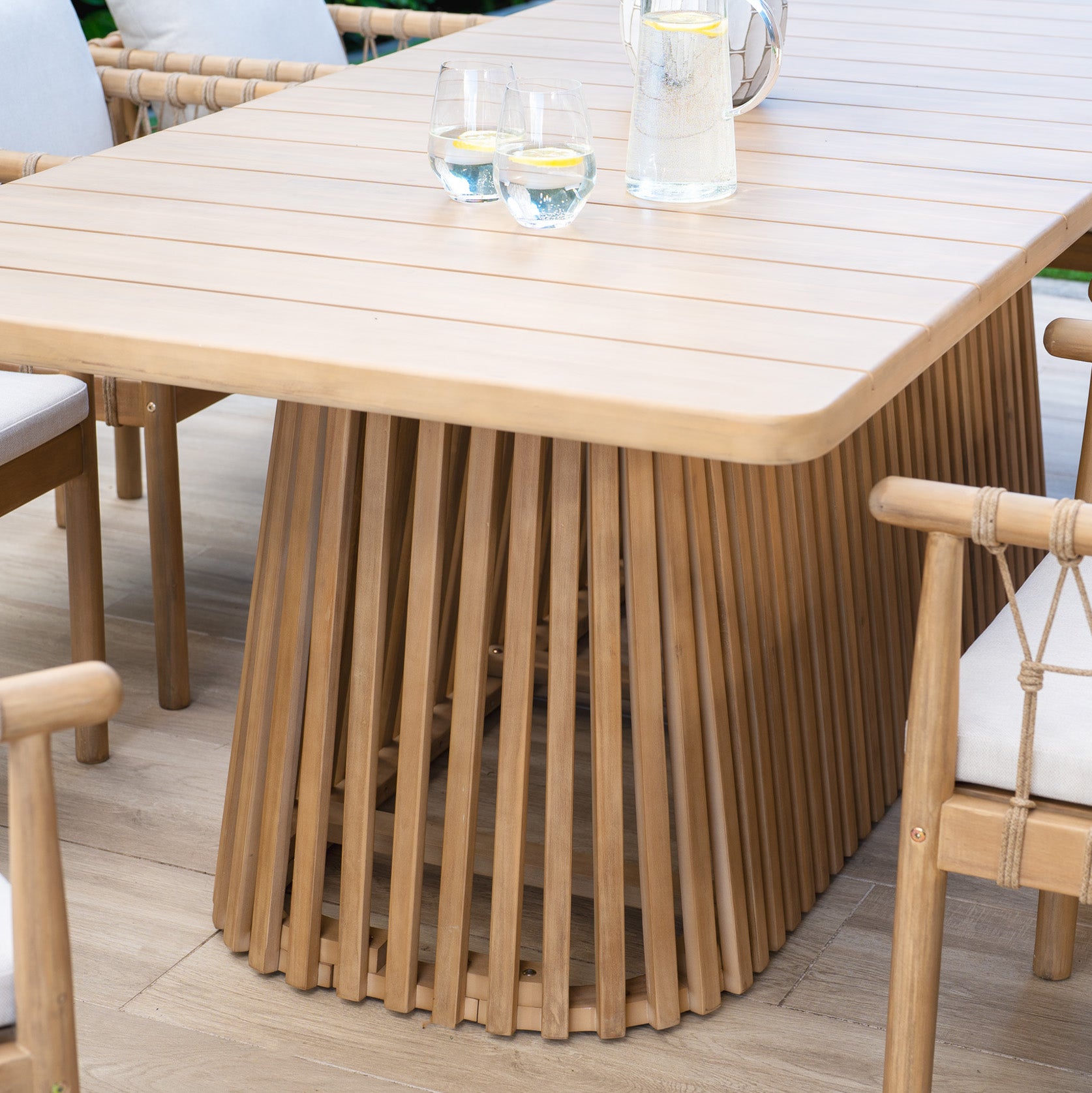 Experience unforgettable outdoor dining with the Paia 8 Seat Rectangular Dining Set in Linen. It includes an Acacia wood table with a slatted base and water-resistant fabric chairs, perfect for enjoying al fresco meals with three glasses and a jug of water on top.