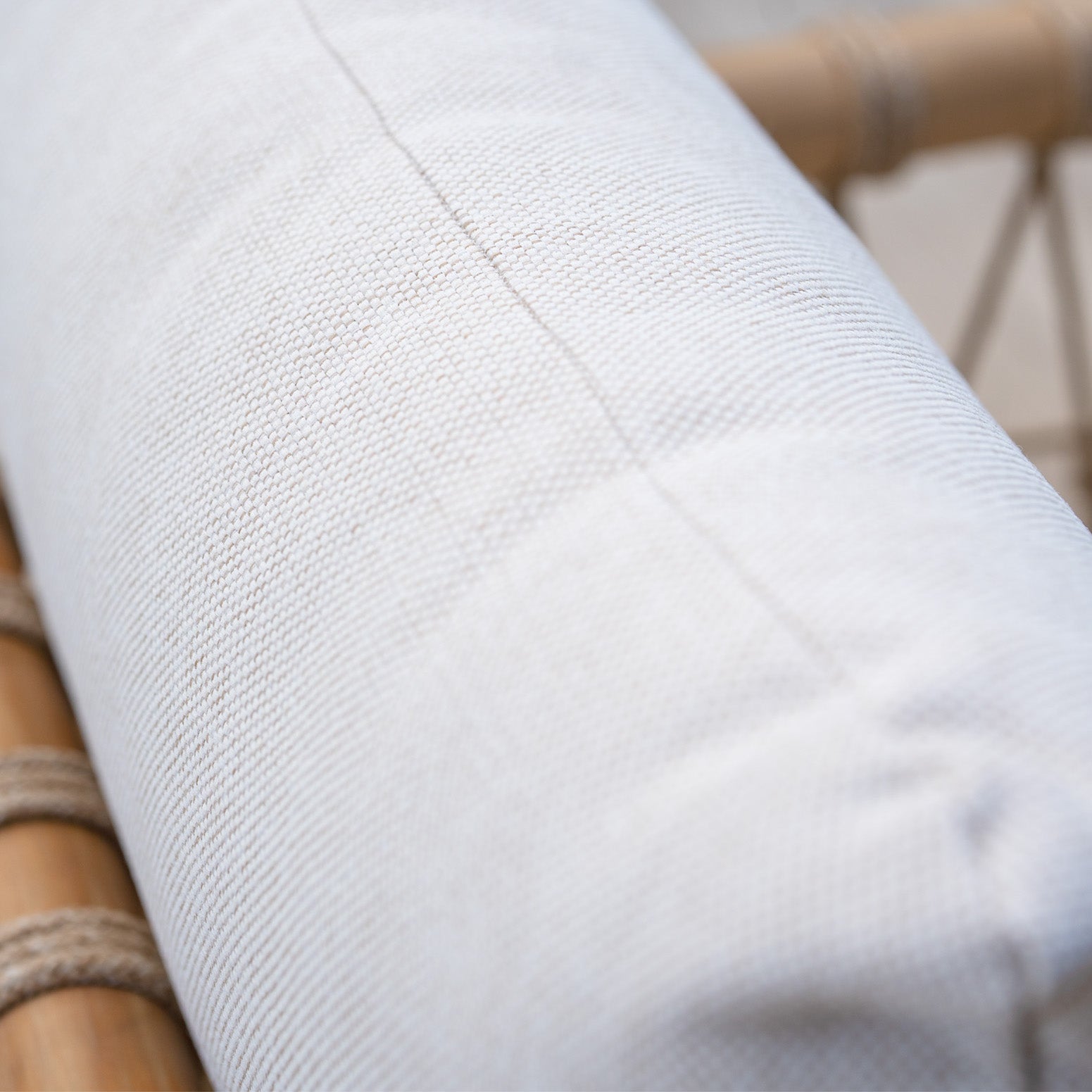 Close-up of a white textured cushion made from water-resistant fabric on a wooden chair with woven rope accents, ideal for the Paia 8 Seat Rectangular Dining Set in Linen.