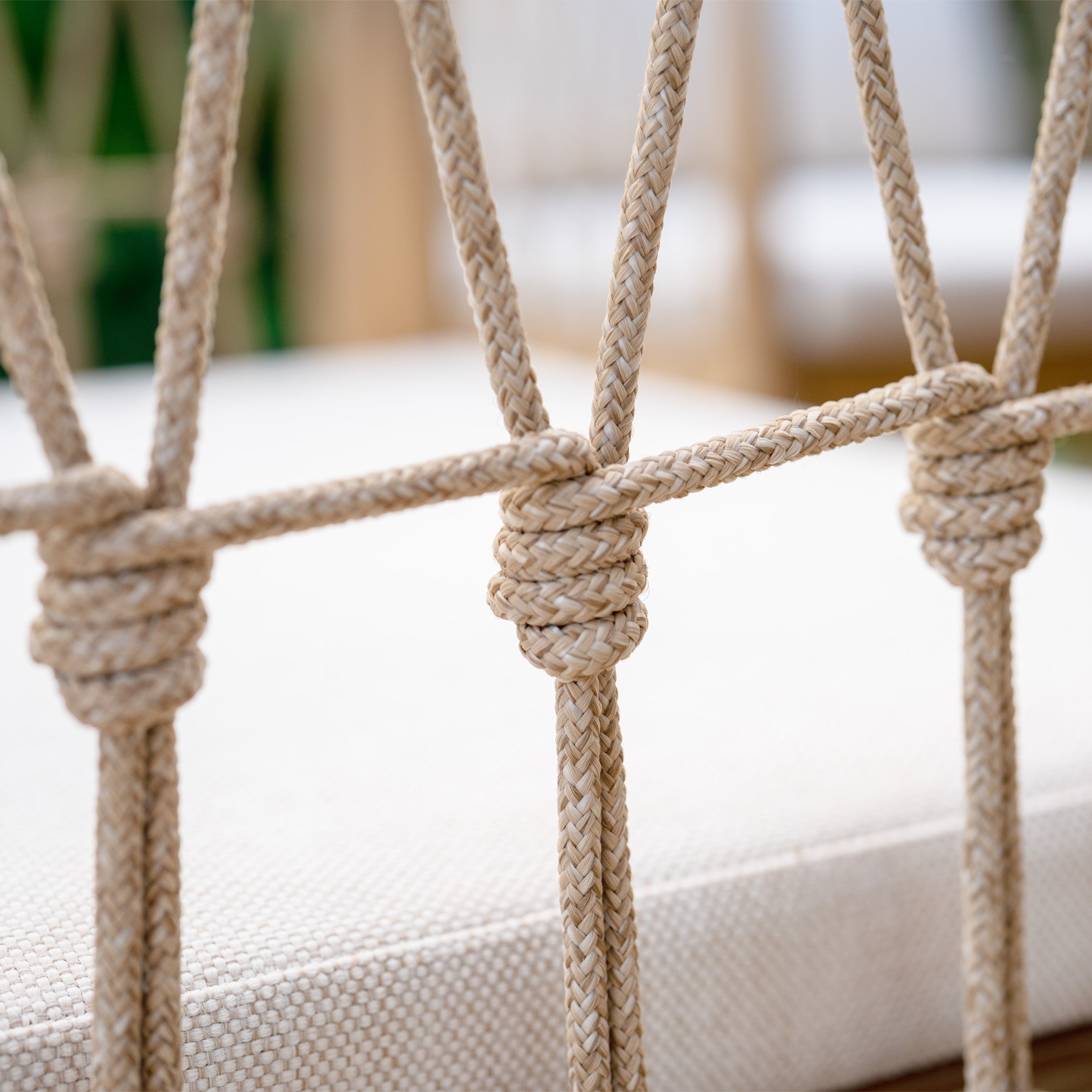 Close-up of a beige, intricately knotted rope creating a decorative pattern on a chair back, perfectly complementing the acacia wood frame of the Paia 8 Seat Rectangular Dining Set in Linen.