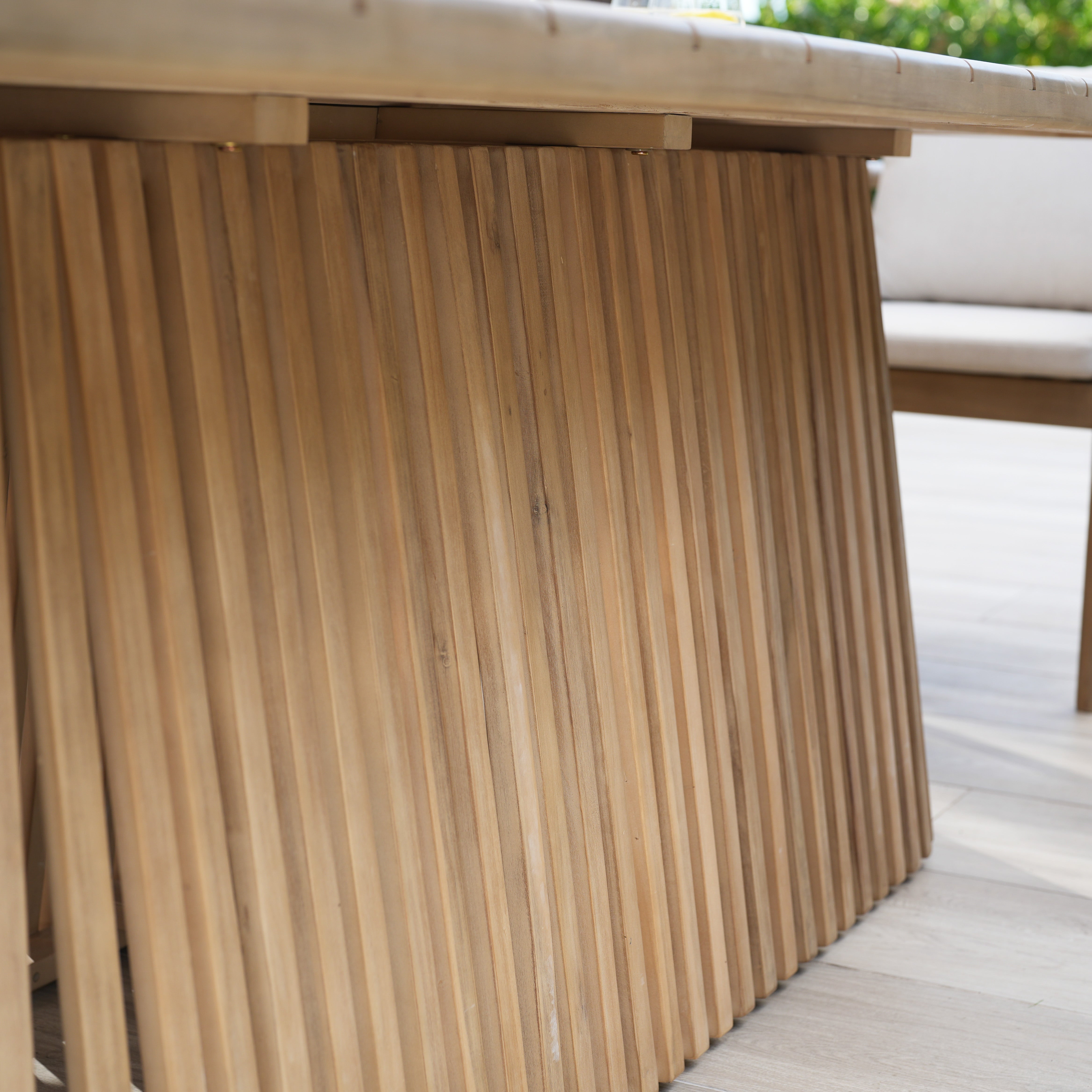 The Paia 8 Seat Rectangular Dining Set in Linen, crafted from sustainably sourced Acacia wood with a slatted design, sits elegantly on a light-colored tiled floor, perfect for creating an inviting outdoor dining space.