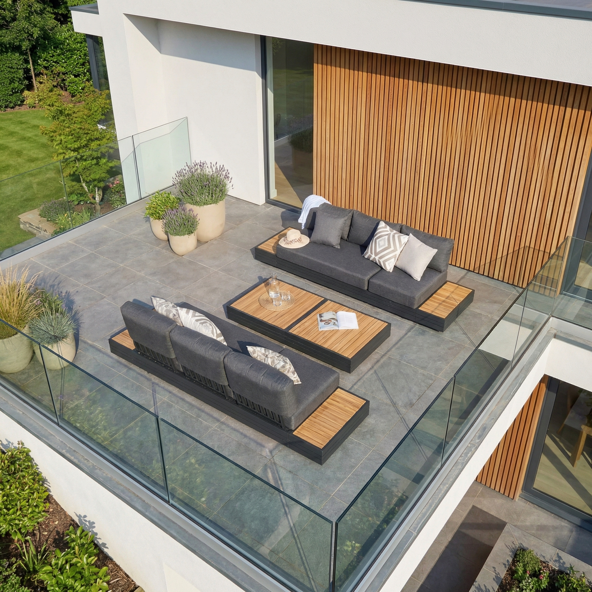 Modern patio with two Panama 3 Seat Sofas with Sun Lounger Feature in Charcoal, cozy cushions, potted plants, a wooden coffee table, and glass railing—ideal for relaxing or pairing with your favorite lounge setup.