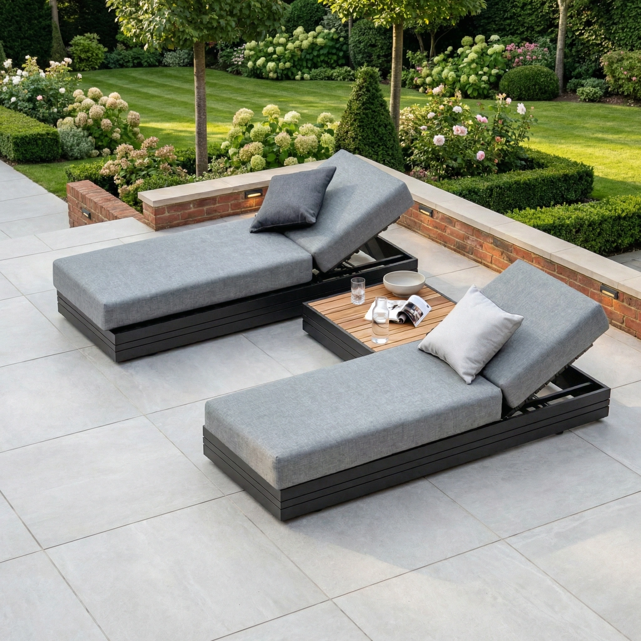 The Panama 3 Seat Sofa with Sun Lounger Feature in washed grey sits on a patio, its stylish design complemented by cushions and pillows, framed by lush garden greenery with shrubs and trees in the background.