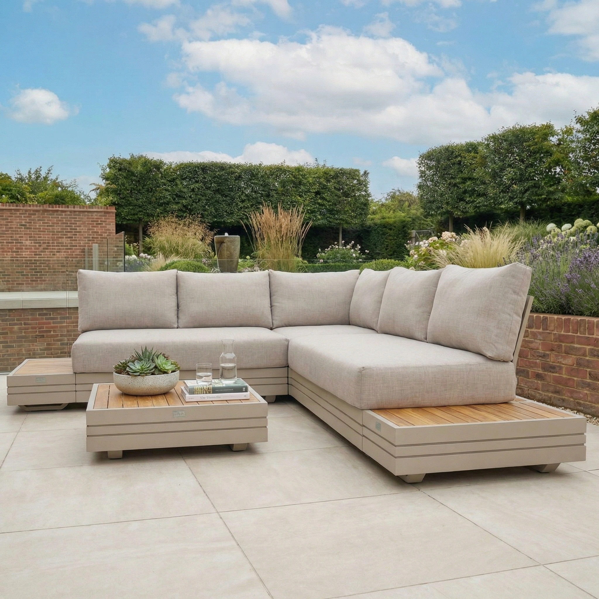 Modern outdoor patio with a Panama Luxury Outdoor Corner Group Set in Latte, coffee table, and plants on large light tiles beneath a blue sky.