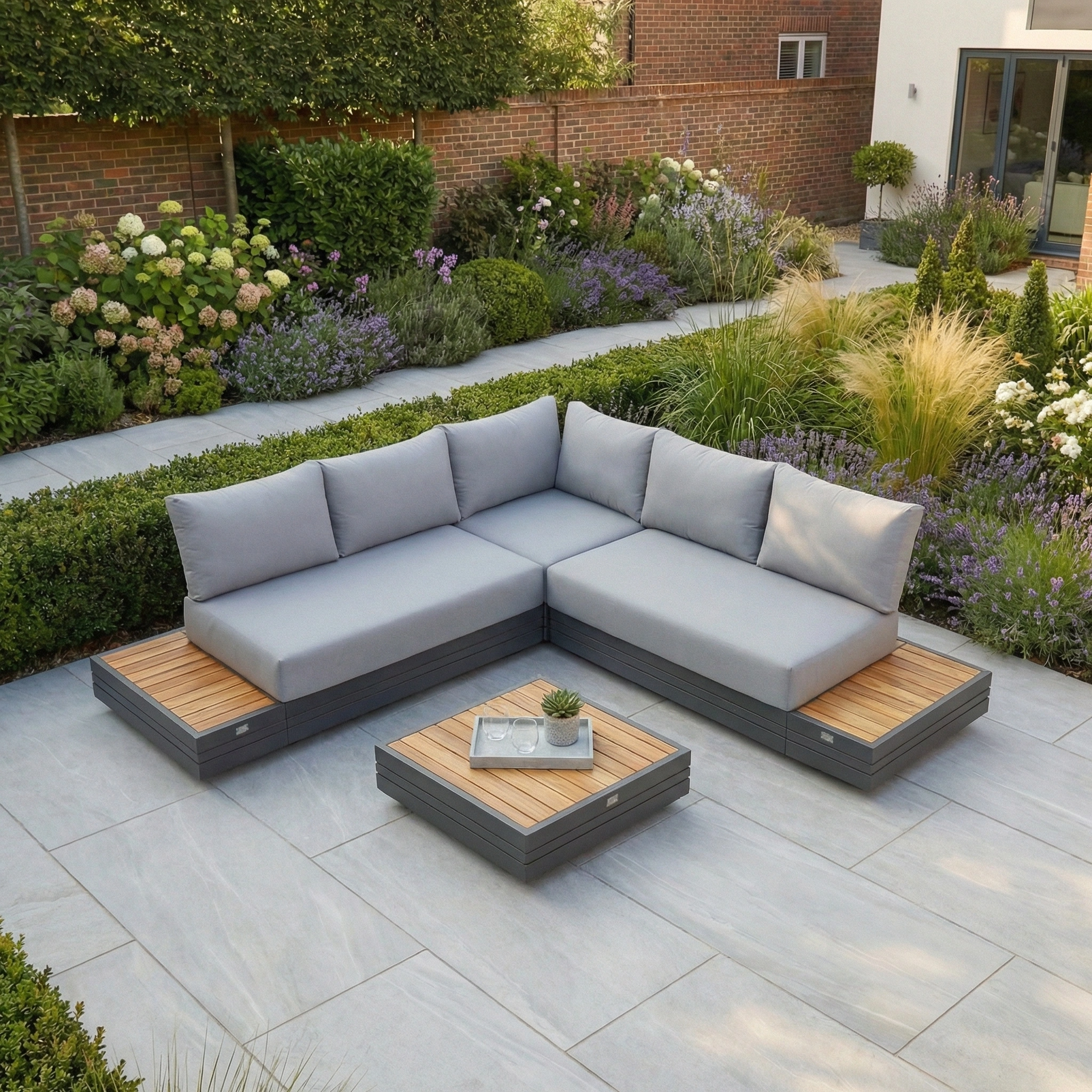 Modern patio with the Panama Luxury Outdoor Corner Group Set in Washed Grey and a small table, surrounded by lush garden greenery for a relaxing atmosphere.
