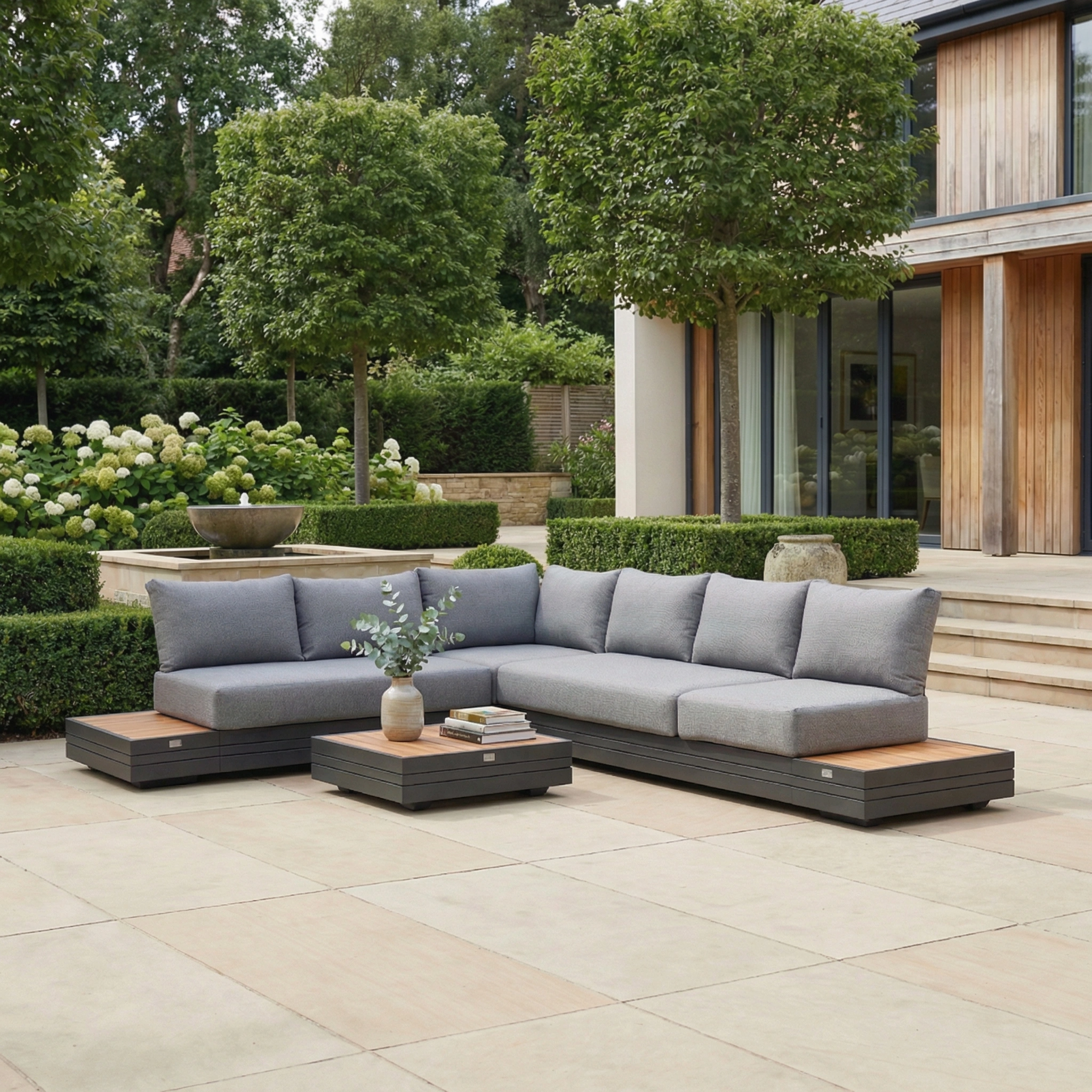 A modern patio showcases the Panama Luxury Outdoor L-Shape Corner Group Set in Washed Grey, paired with low tables and lush greenery, featuring sustainable teak furniture for an eco-conscious and stylish garden setting.