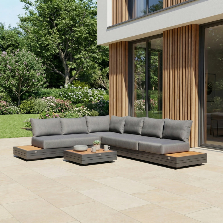 Modern outdoor patio featuring the Panama Luxury Outdoor L-Shape Corner Group Set in Charcoal, a low coffee table, and a lush green garden in the background.