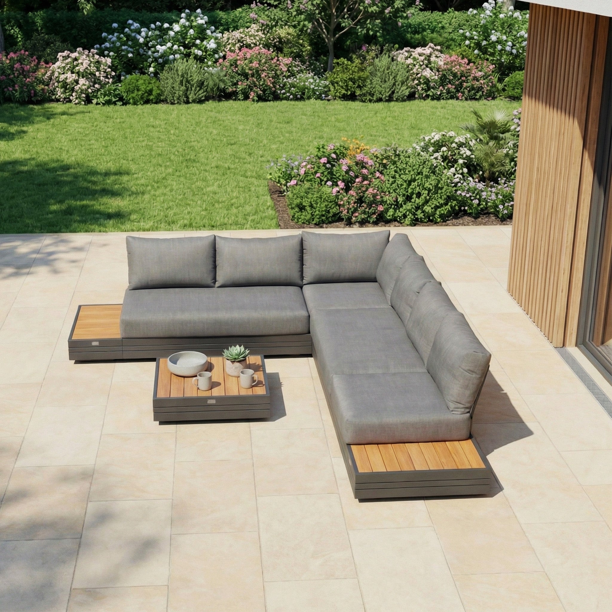 The Panama Luxury Outdoor L-Shape Corner Group Set in Charcoal features a weatherproof aluminium sofa and coffee table, stylishly arranged on a tiled patio with a green lawn and garden backdrop for lasting outdoor elegance.