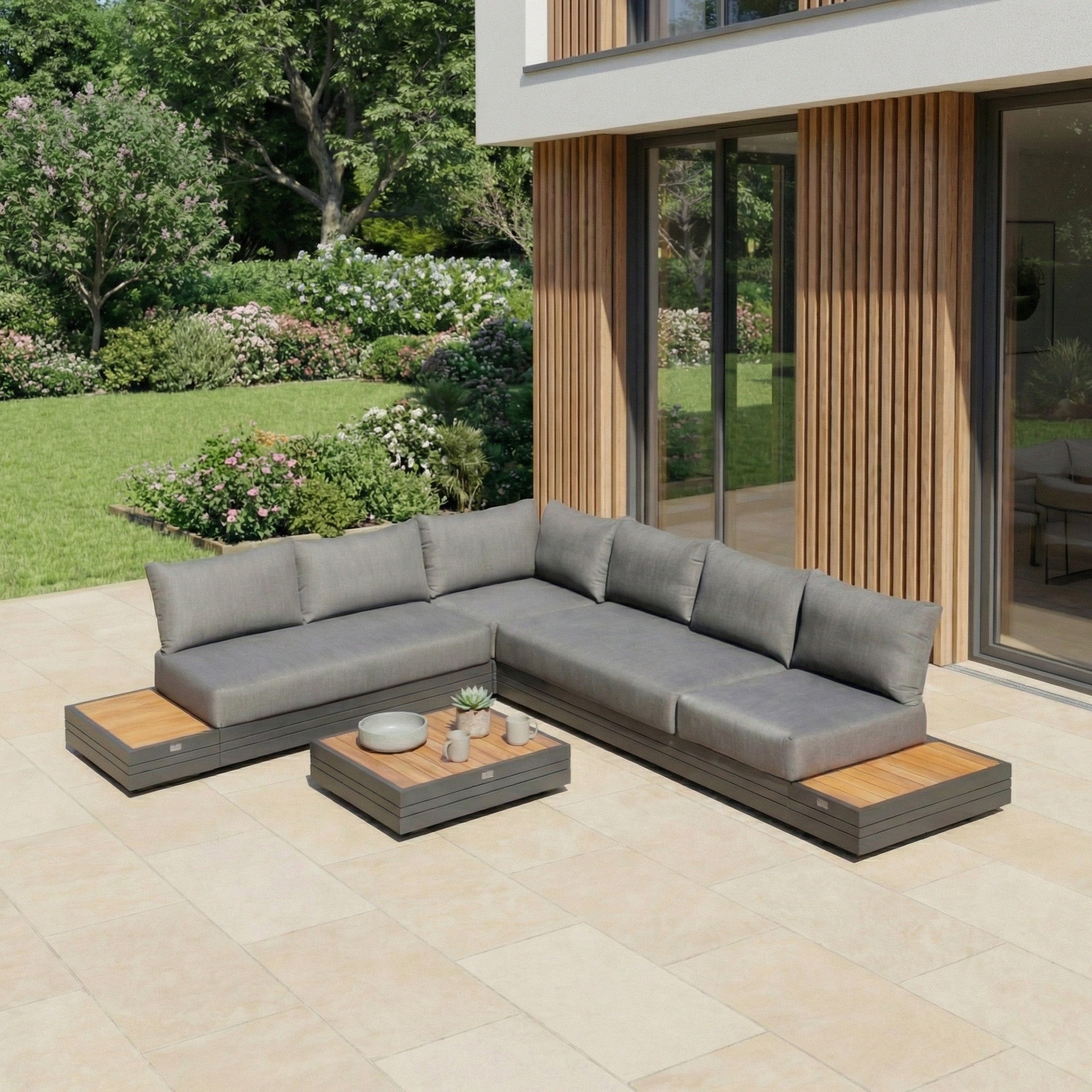 Modern outdoor patio featuring the Panama Luxury Outdoor L-Shape Corner Group Set in Charcoal, wooden accents, and a low table, surrounded by greenery for a stylish and relaxing retreat.