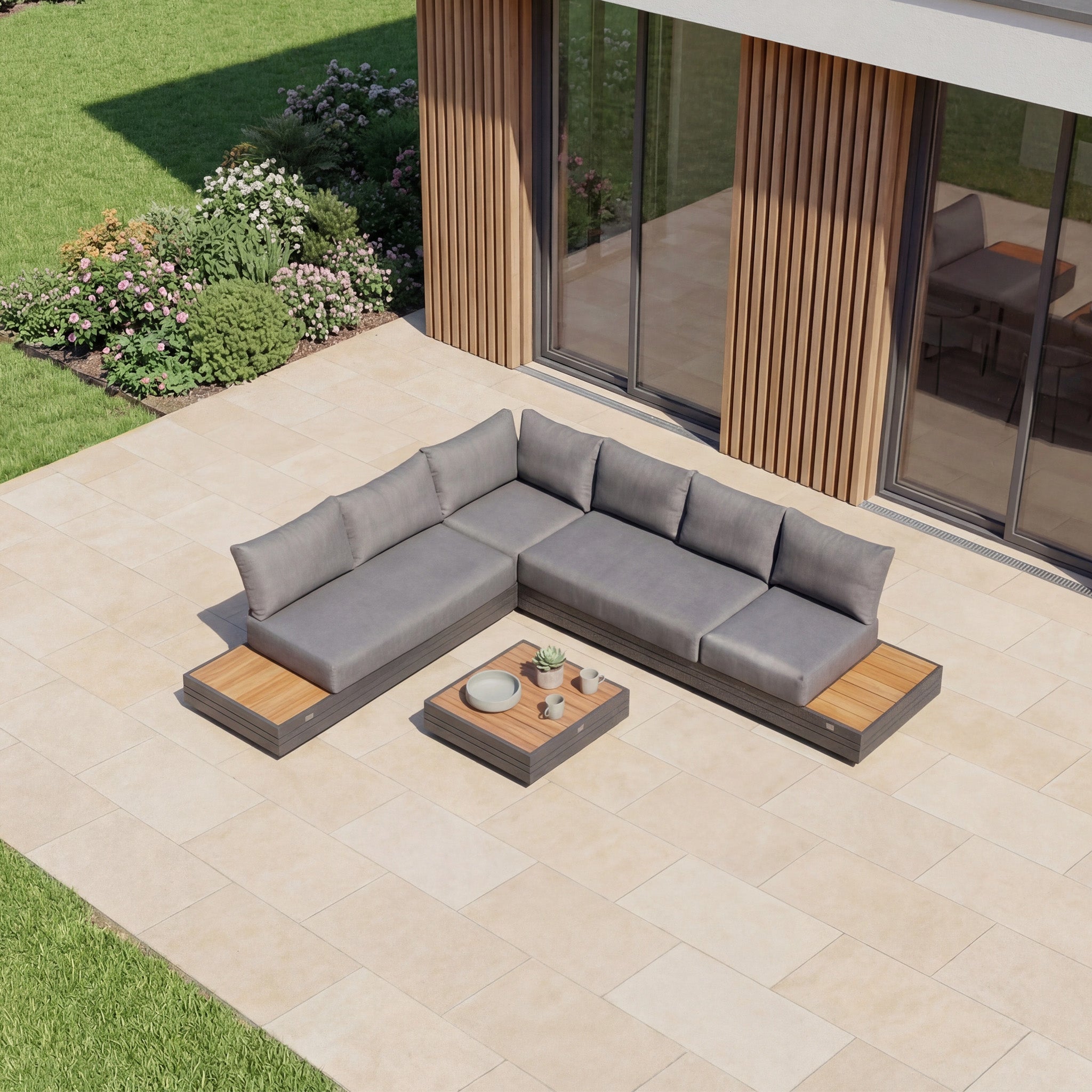 Modern patio with garden views beside a house with large windows, featuring the Panama Luxury Outdoor L-Shape Corner Group Set in Charcoal and coffee table.
