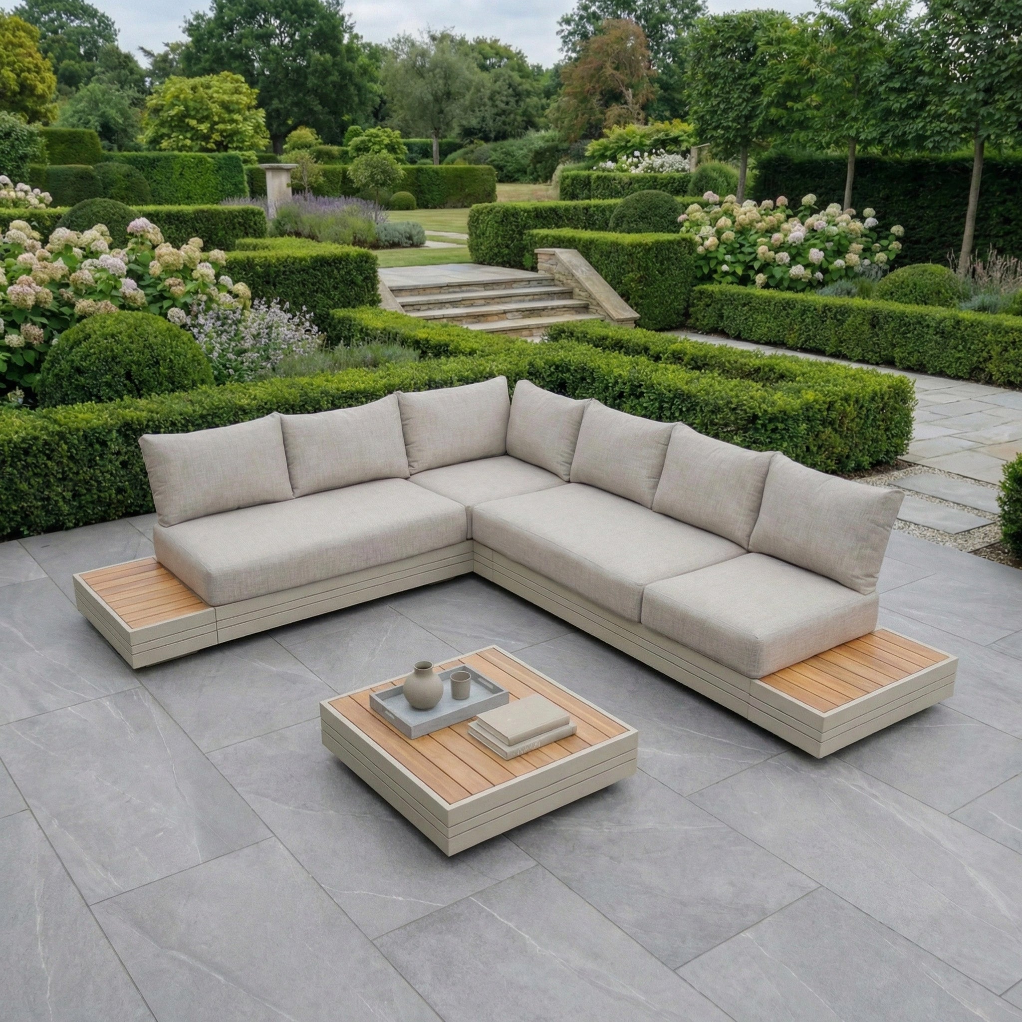 Modern latte outdoor L-shape sectional and coffee table from the Panama Luxury Outdoor L-Shape Corner Group Set in Latte on a large stone patio in a landscaped garden.