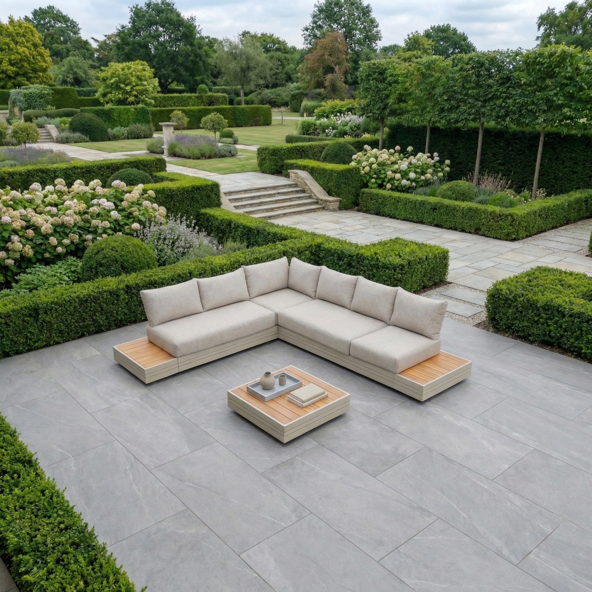 Modern patio with the Panama Luxury Outdoor L-Shape Corner Group Set in Latte and coffee table, surrounded by lush gardens, featuring aluminium and sustainable teak furniture for stylish durability.