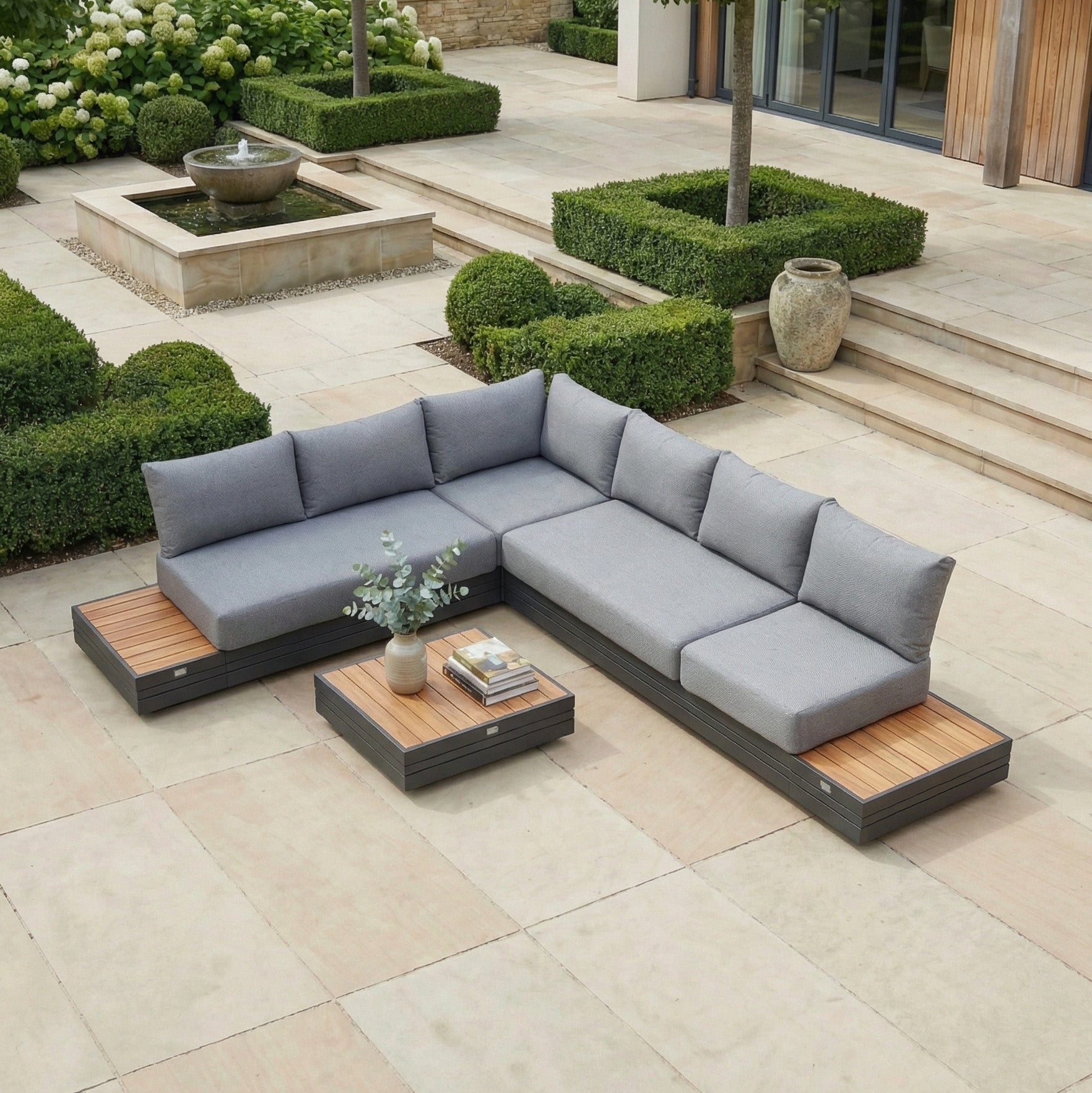 The Panama Luxury Outdoor L-Shape Corner Group Set in Washed Grey creates a modern patio look, paired with a sustainable teak table, potted plant, and trimmed hedges—an ideal blend of style and comfort for your garden.