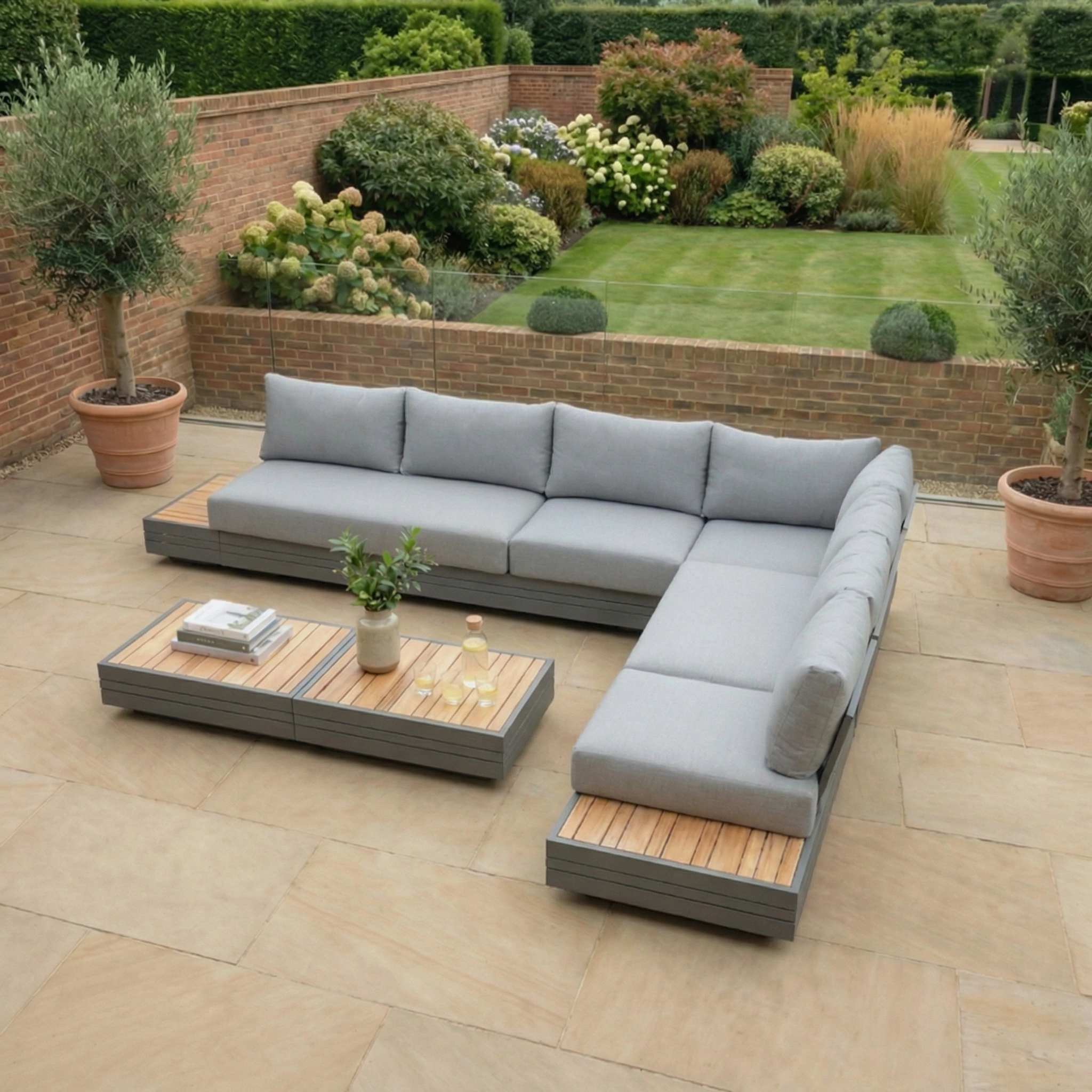 Panama Luxury Outdoor Large Corner Group Set in Washed Grey with coffee table on a stone patio, surrounded by potted trees and a landscaped garden.