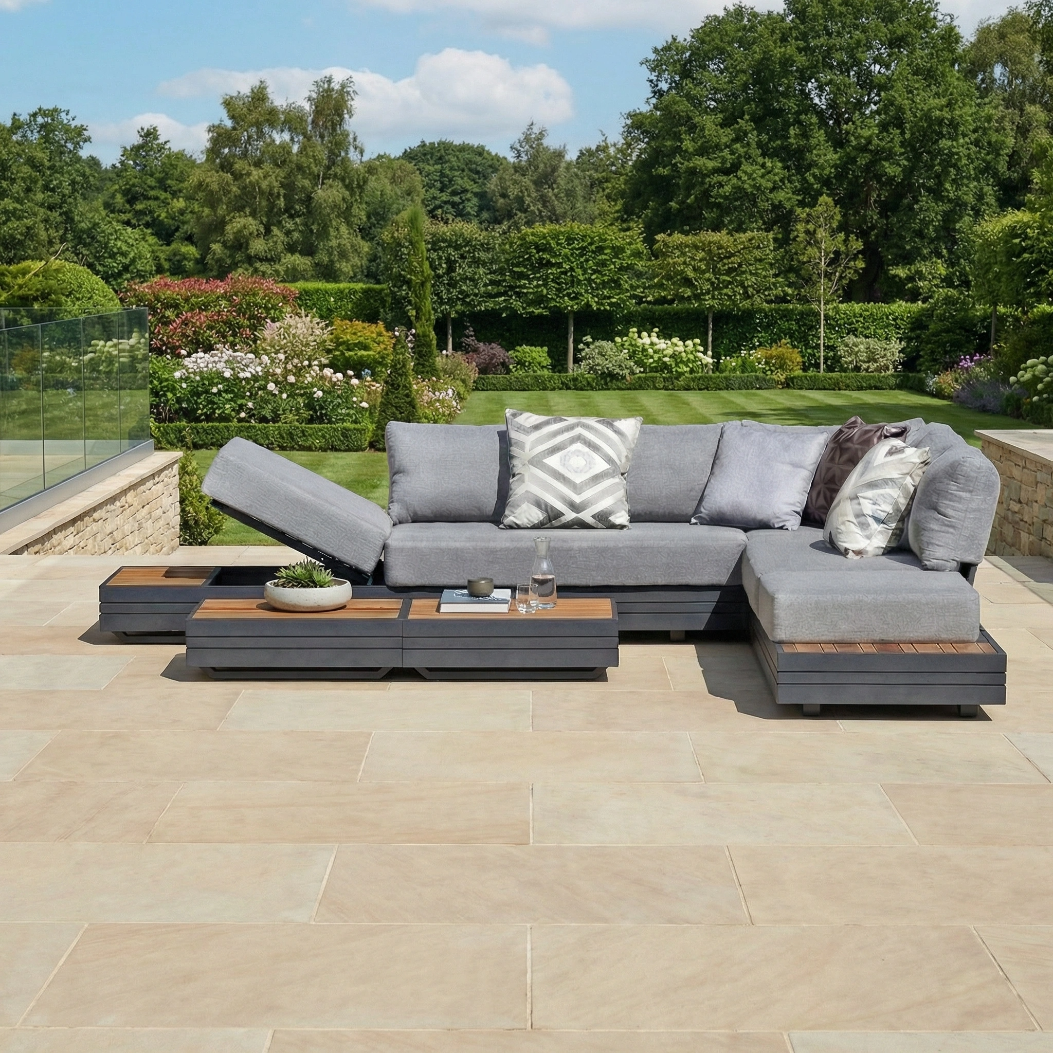 The Panama Luxury Outdoor Large Corner Group Set in Washed Grey features cushions and pillows, arranged on a tiled patio with views of a lush green garden.