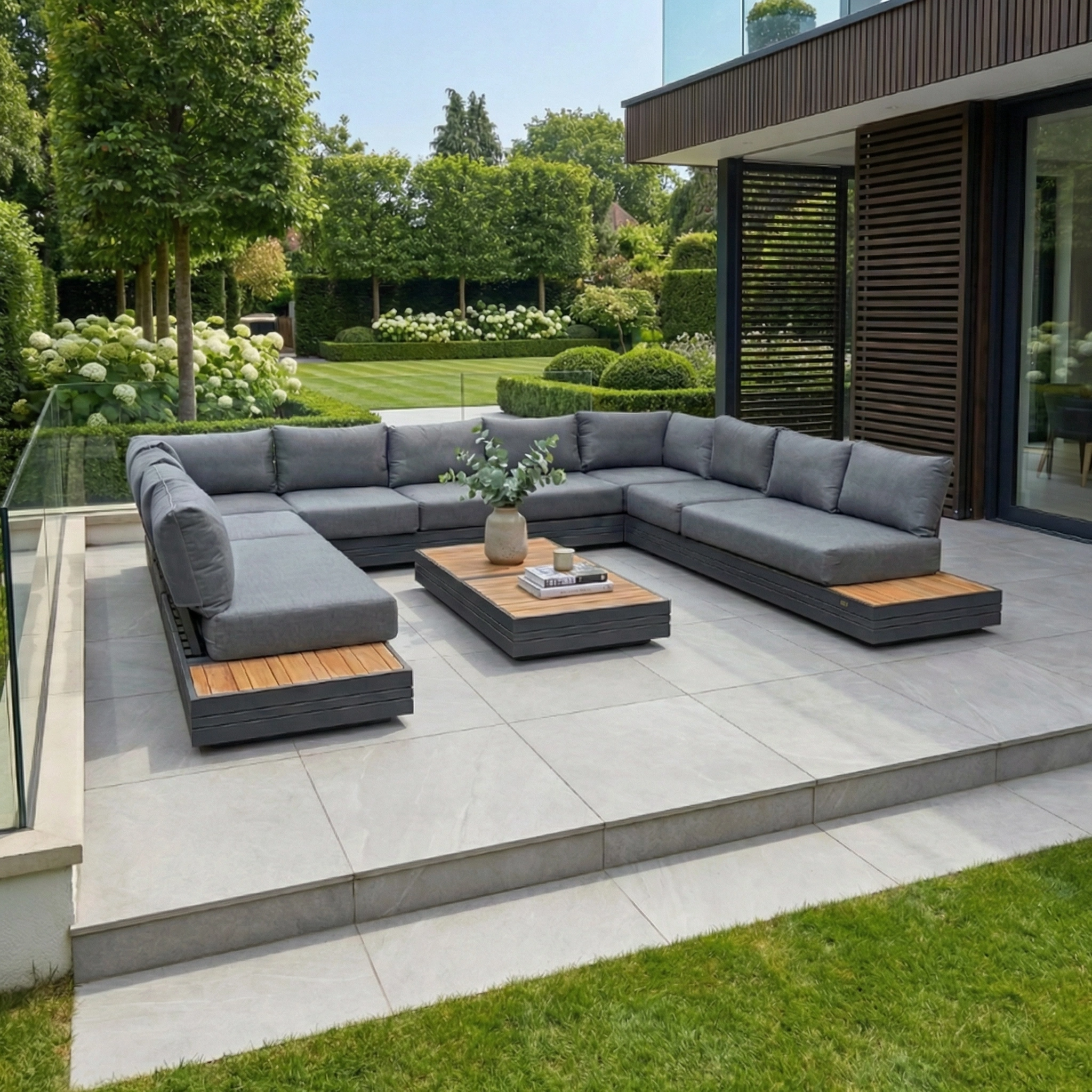 Modern patio with the Panama Luxury Outdoor Large U-Shape Corner Sofa Set in Charcoal, a sustainable teak coffee table, and a lush green garden in the background.