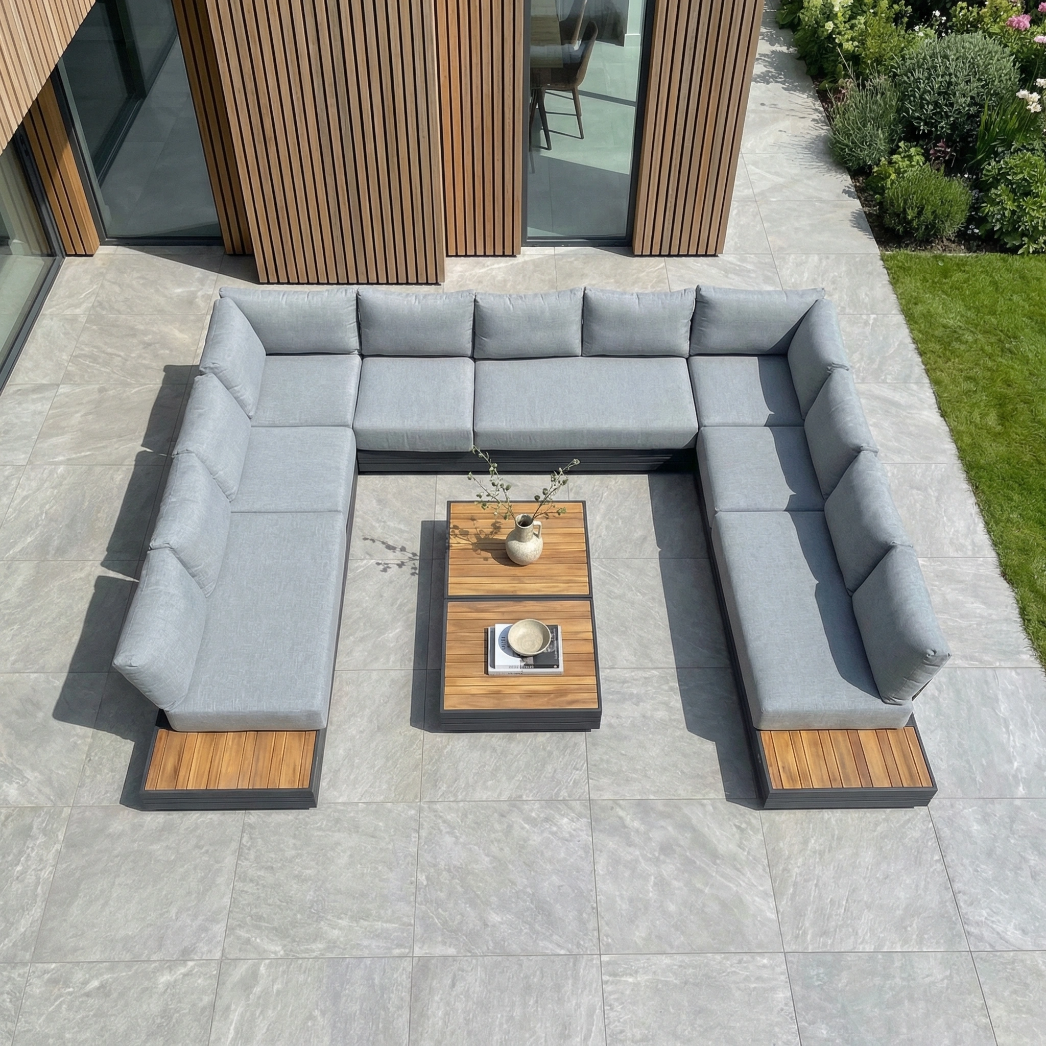 The Panama Luxury Outdoor Large U-Shape Corner Sofa Set in Washed Grey offers stylish outdoor seating, perfect for placing on a stone patio beside a modern house and pairing with a sustainable teak coffee table.