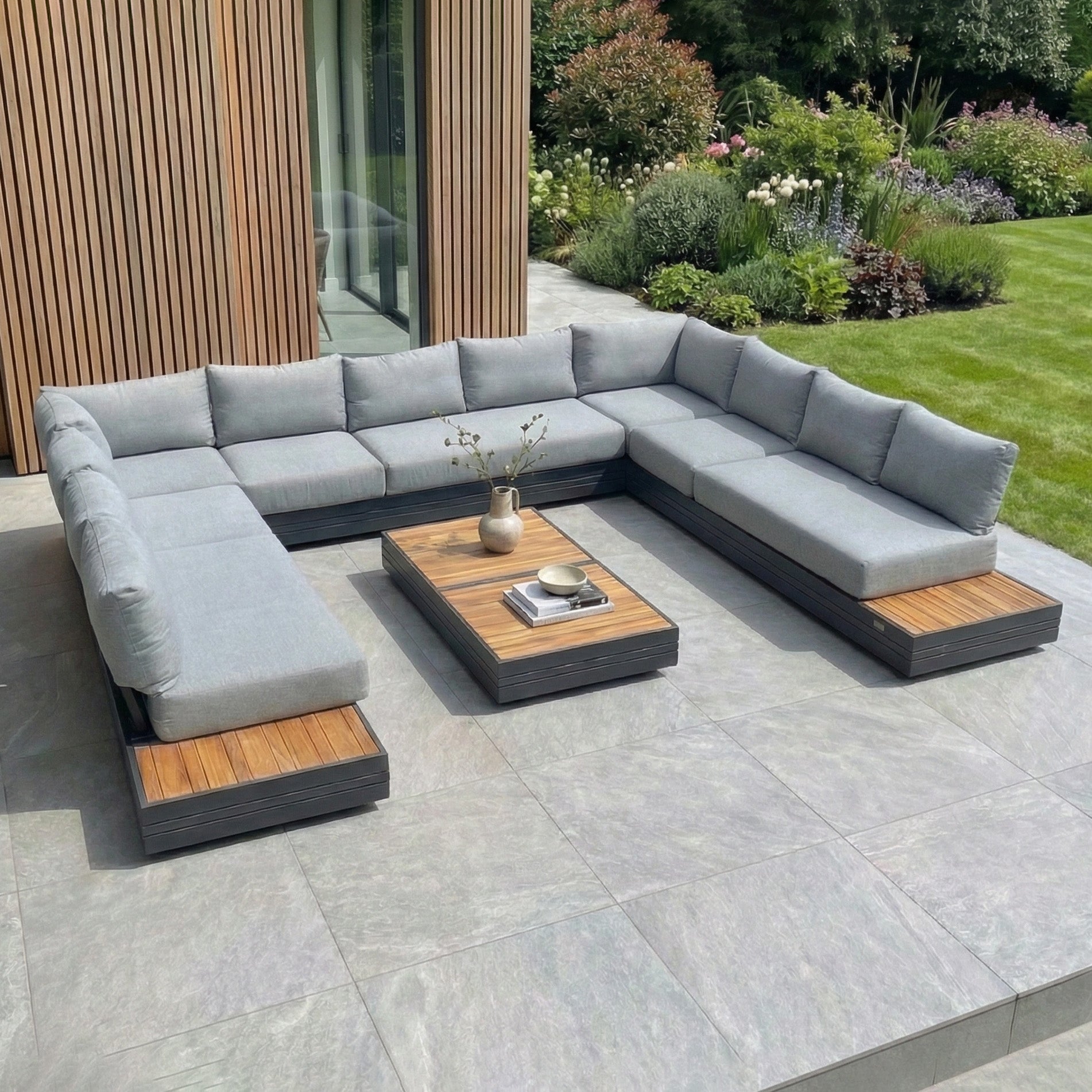 Modern patio with the Panama Luxury Outdoor Large U-Shape Corner Sofa Set in Washed Grey, sustainable teak coffee tables, and a landscaped garden—this stylish set elevates any backyard retreat.